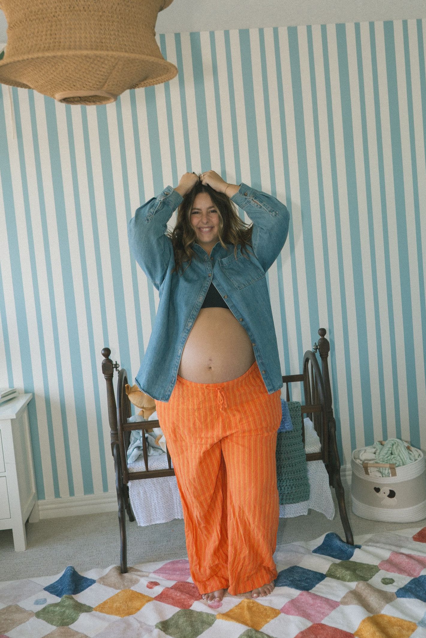 A person wearing a teal sweater and orange pants poses playfully on a colorful patchwork quilt.