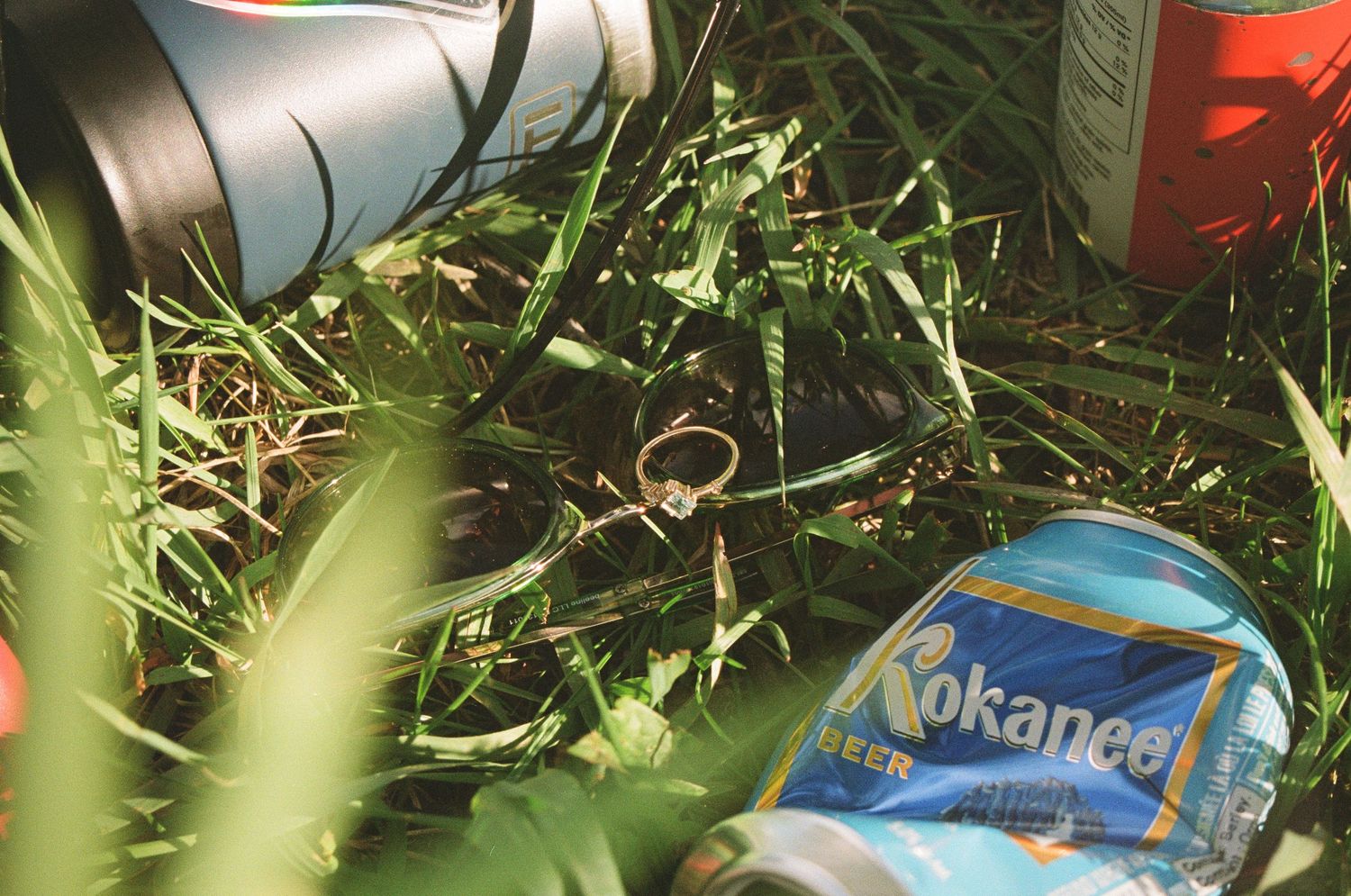 A crushed Yokohama beverage can lies among grass and foliage in an outdoor setting.