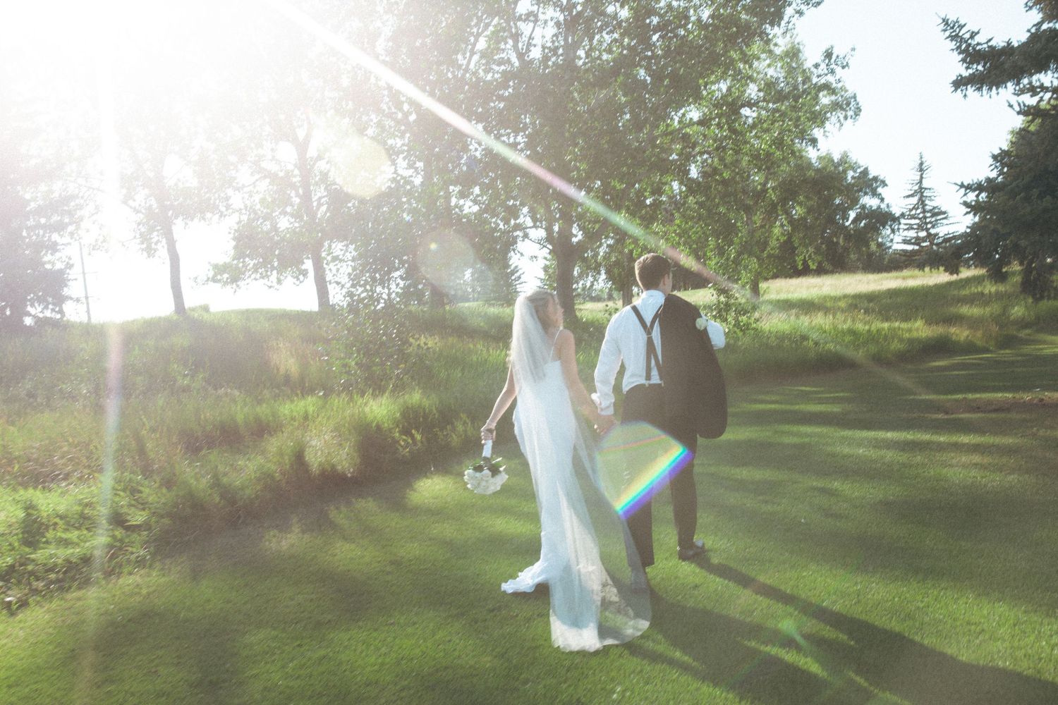 A couple walks together on a sunlit hill during their wedding photoshoot.