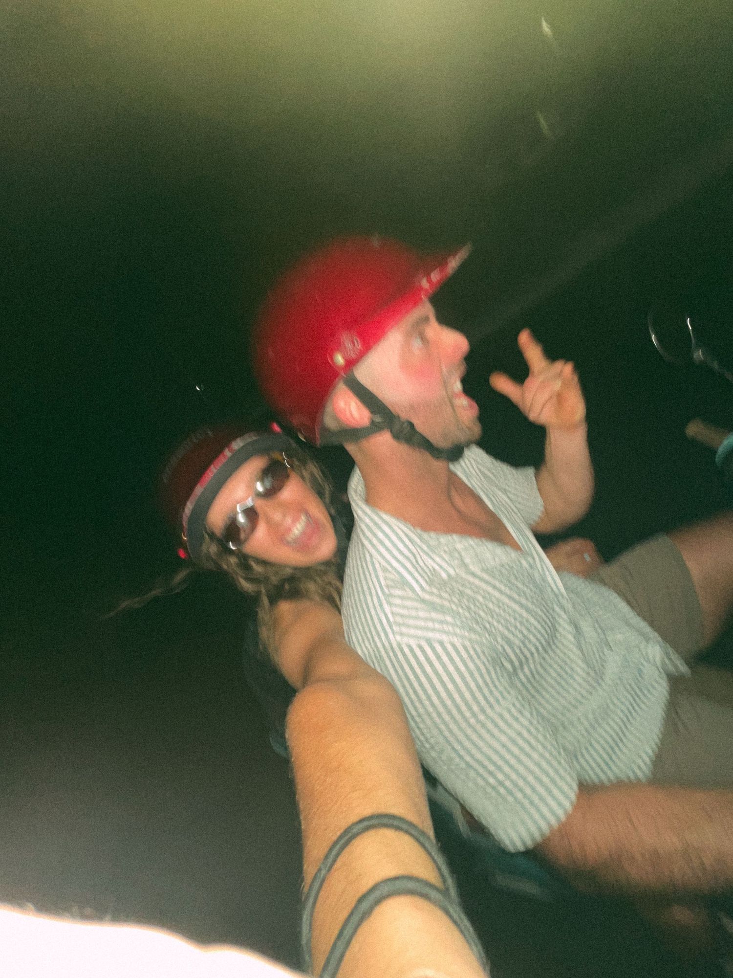 Two people wearing helmets making playful poses in a dimly lit setting.