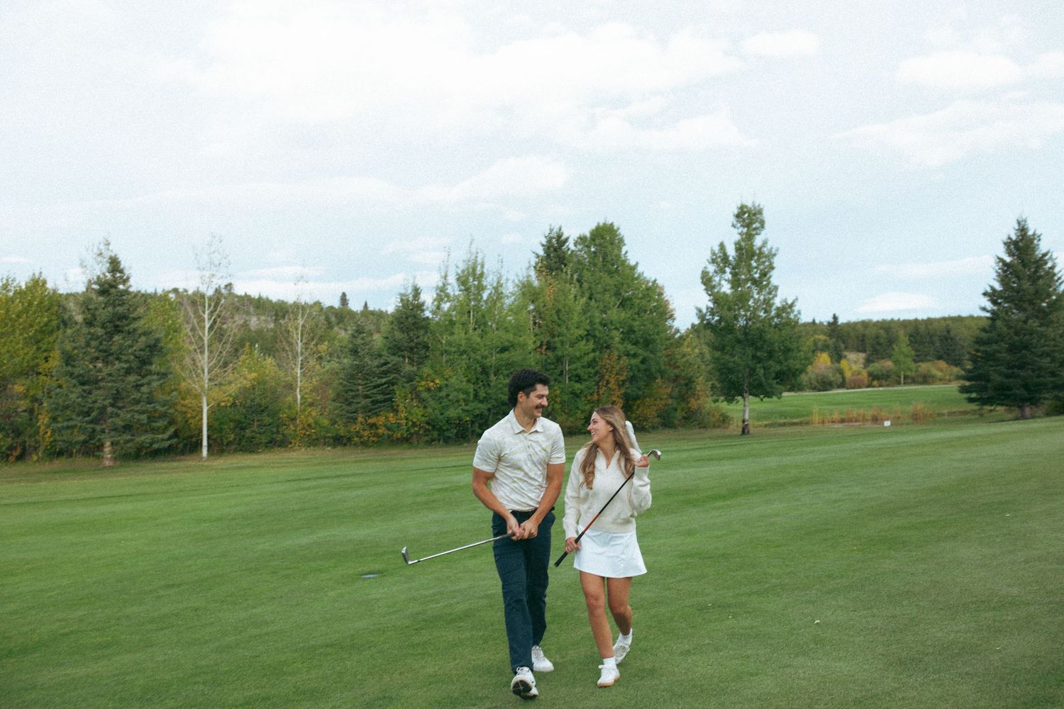 Two people walking together on a lush green golf course fairway on a sunny day.