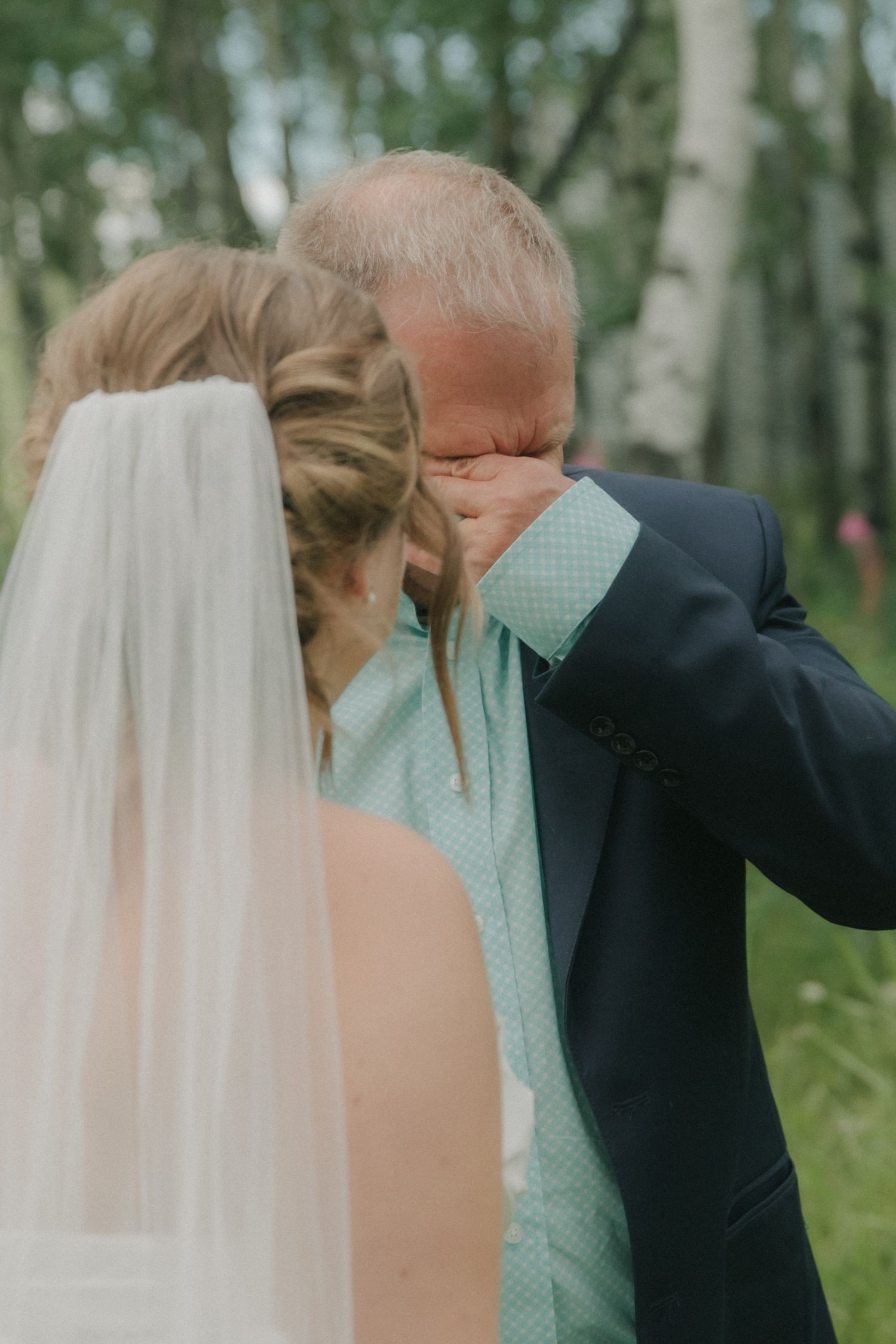 Emotional father wiping tears during outdoor wedding ceremony in birch forest.
