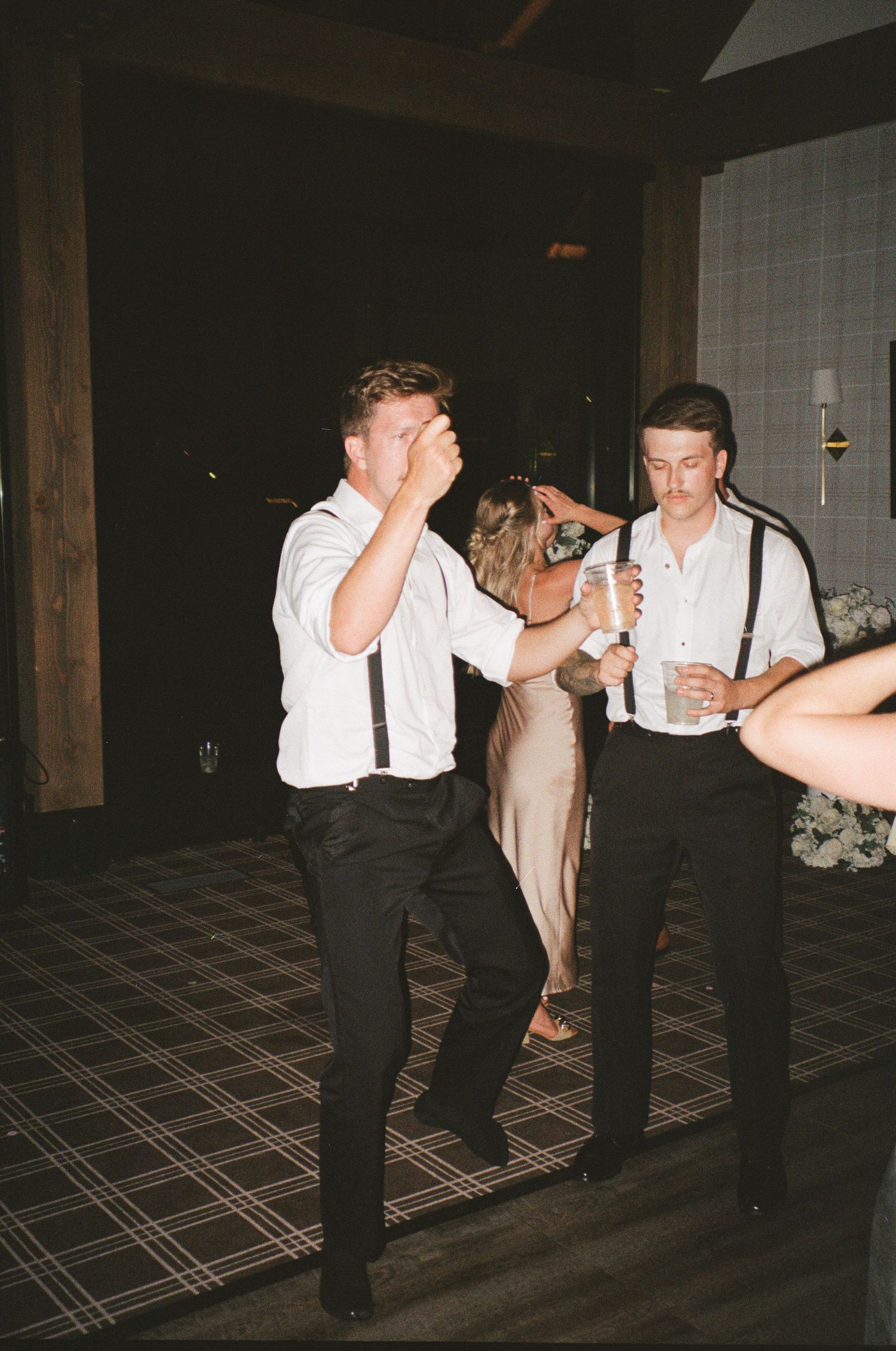 People in formal attire dancing and socializing at what appears to be a wedding reception on a patterned floor.