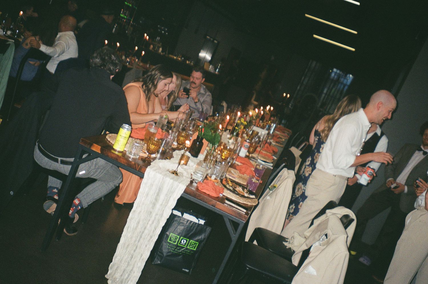 People seated at a dimly lit dinner table with candles and drinks at what appears to be a festive evening event.