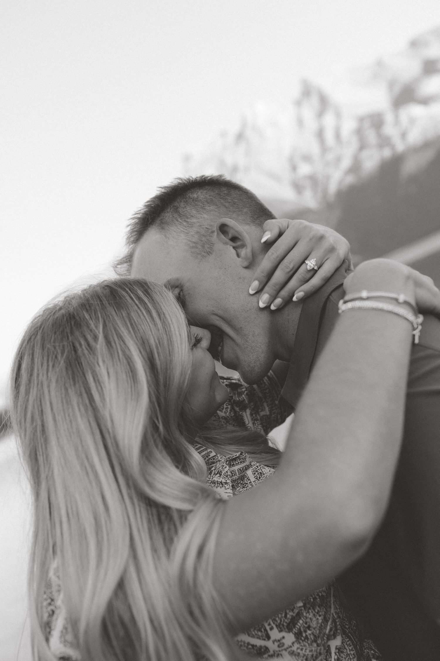 A romantic black and white photo shows a couple embracing in an intimate moment outdoors.