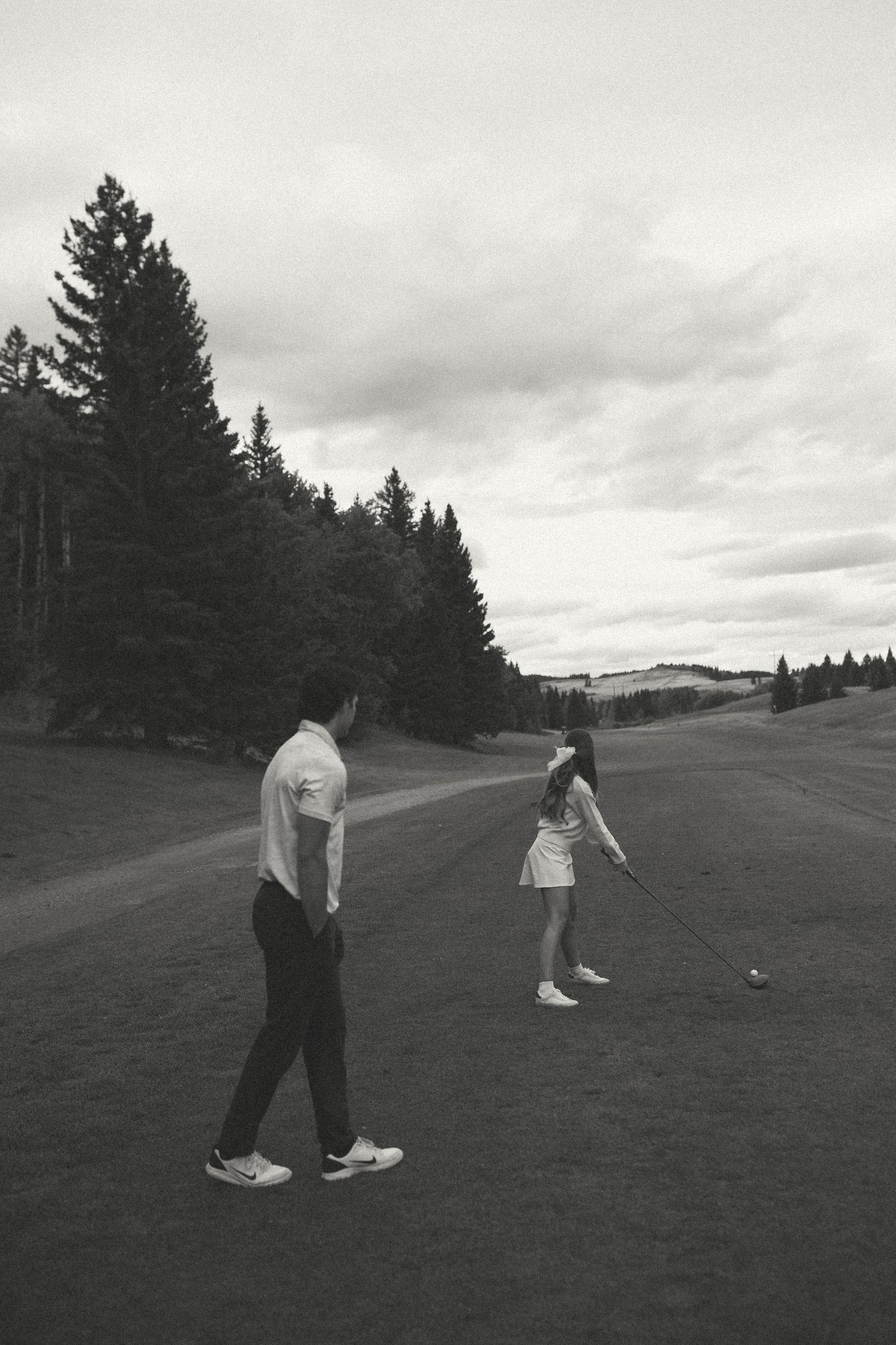 Couple playing golf together on scenic course in black and white.