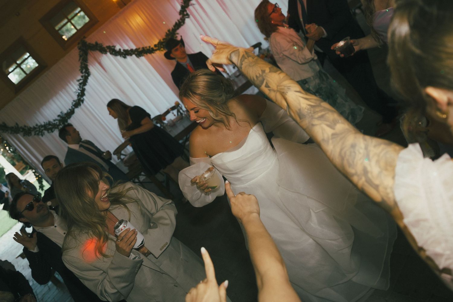 Wedding guests dancing and celebrating on a dimly lit dance floor.