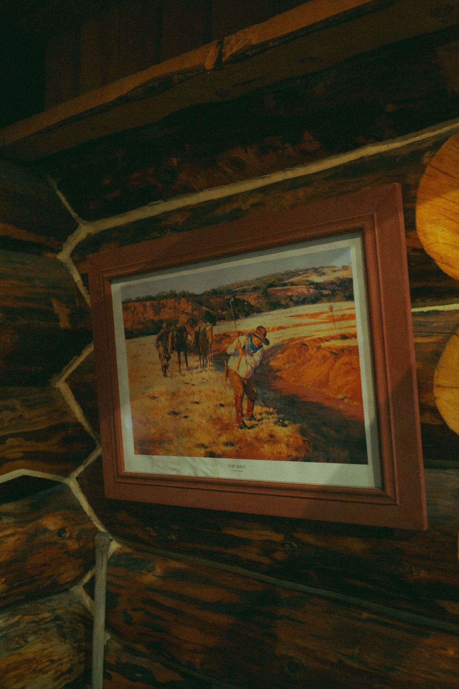 Framed western art print hanging on rustic log cabin wall.