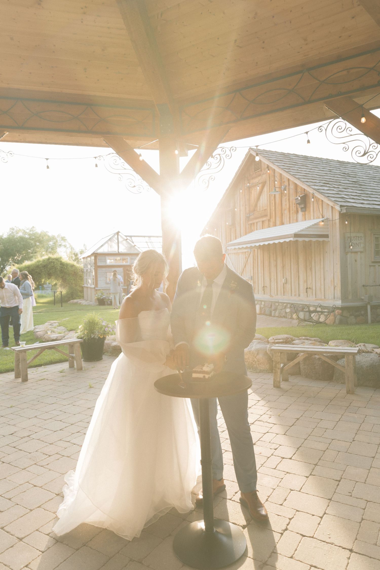 Wedding couple dances in golden sunlight on a stone patio outside a rustic venue.
