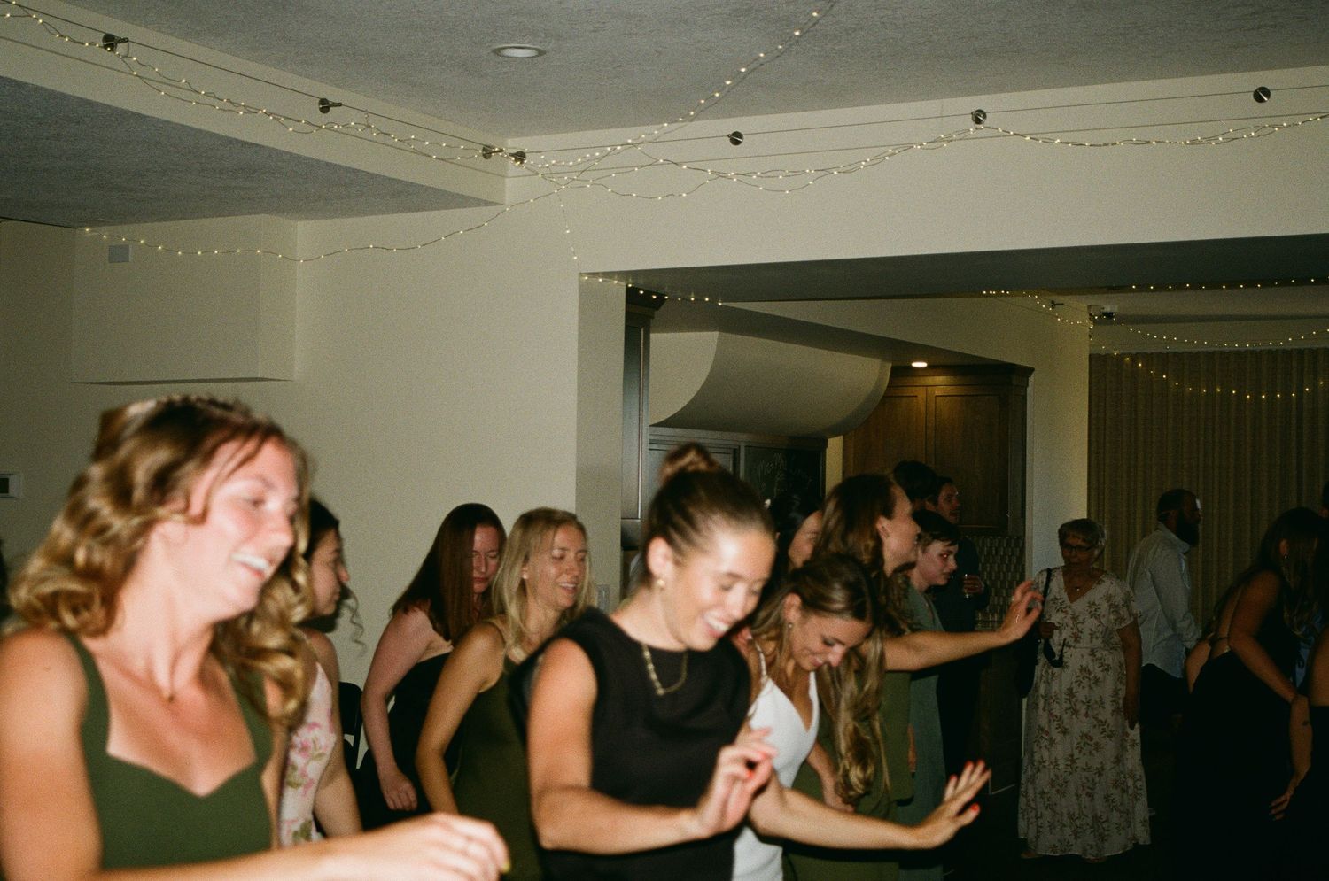Group of women dancing and socializing at an indoor party or wedding reception in elegant attire.