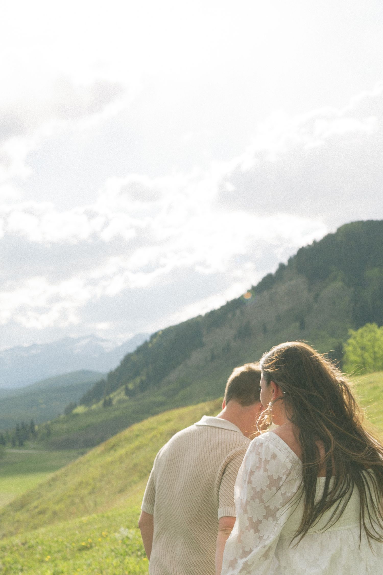 Two people enjoying a scenic mountain view on a grassy hillside on a cloudy day.