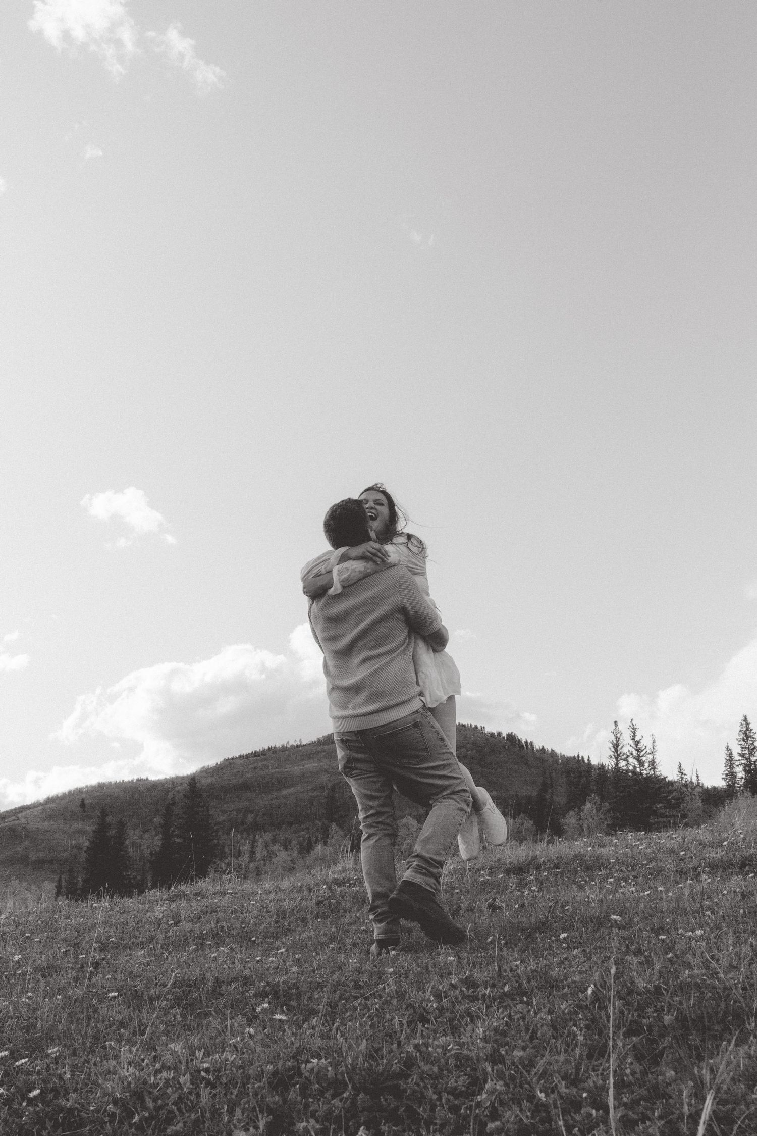 A black and white photograph captures an embrace on a scenic mountain hillside.