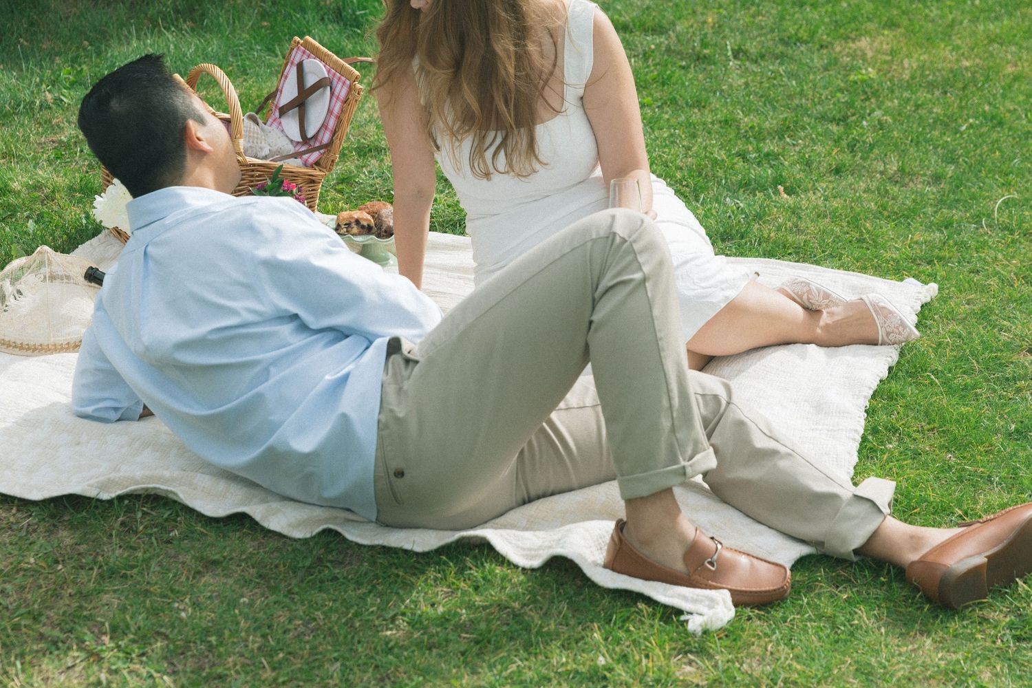 Couple relaxing on a picnic blanket on green grass during a sunny outdoor date.