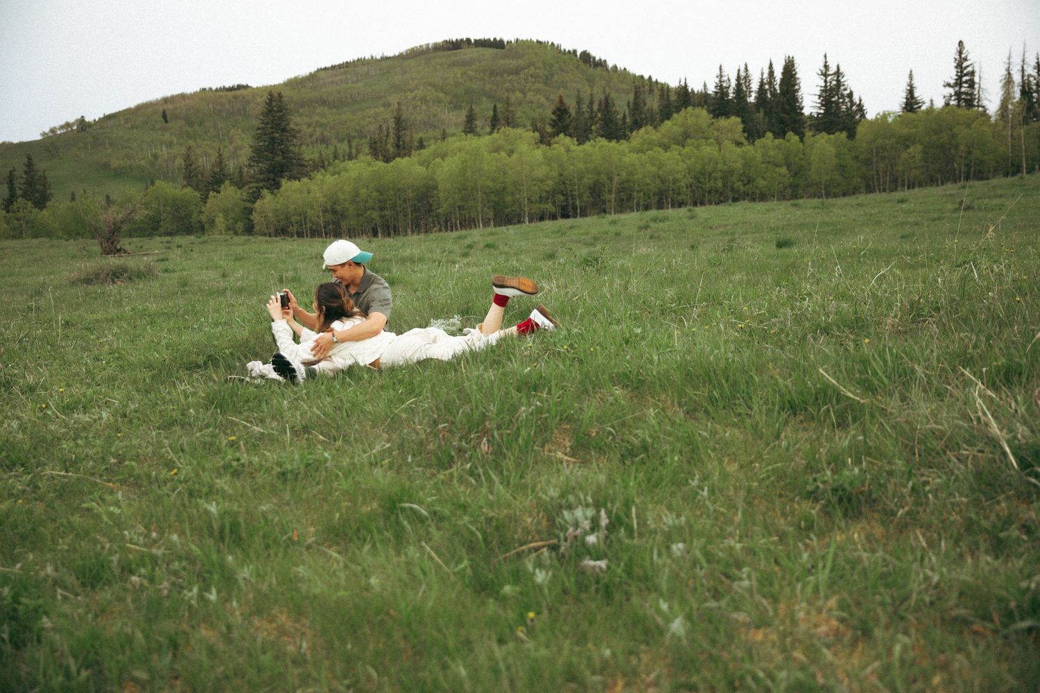 Two people relaxing on a blanket in a scenic mountain meadow.