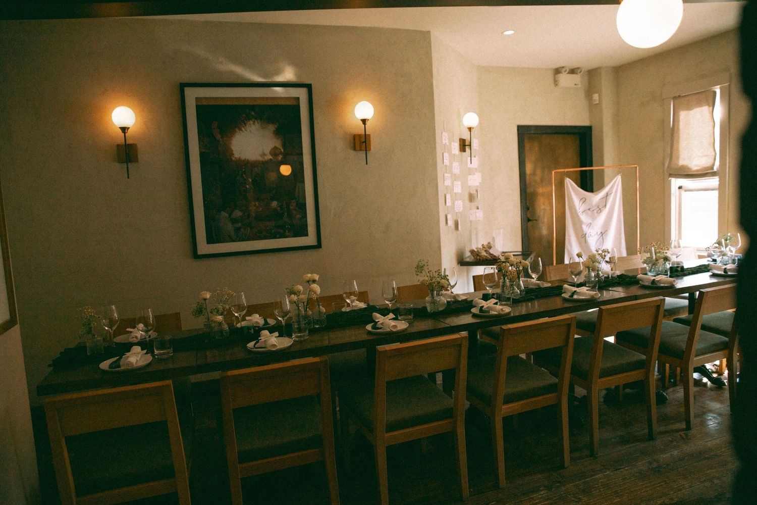 A long wooden dining table set for a formal dinner with wooden chairs and wall sconces in a dimly lit room.