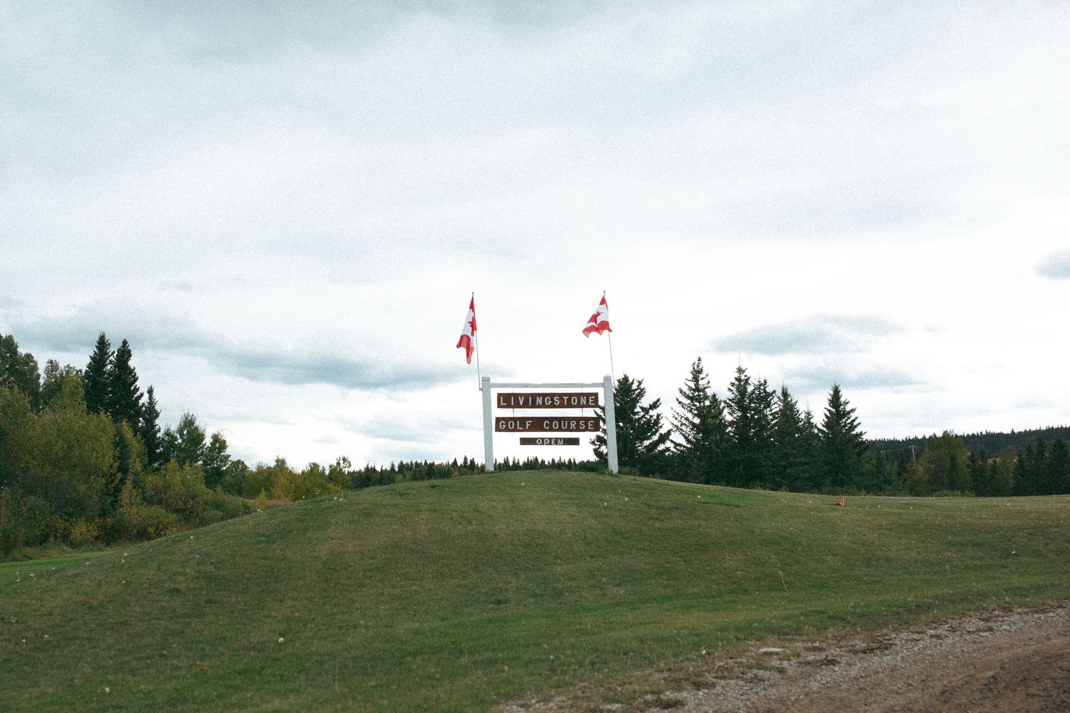 Golf course signage with flags on a hill against cloudy sky.
