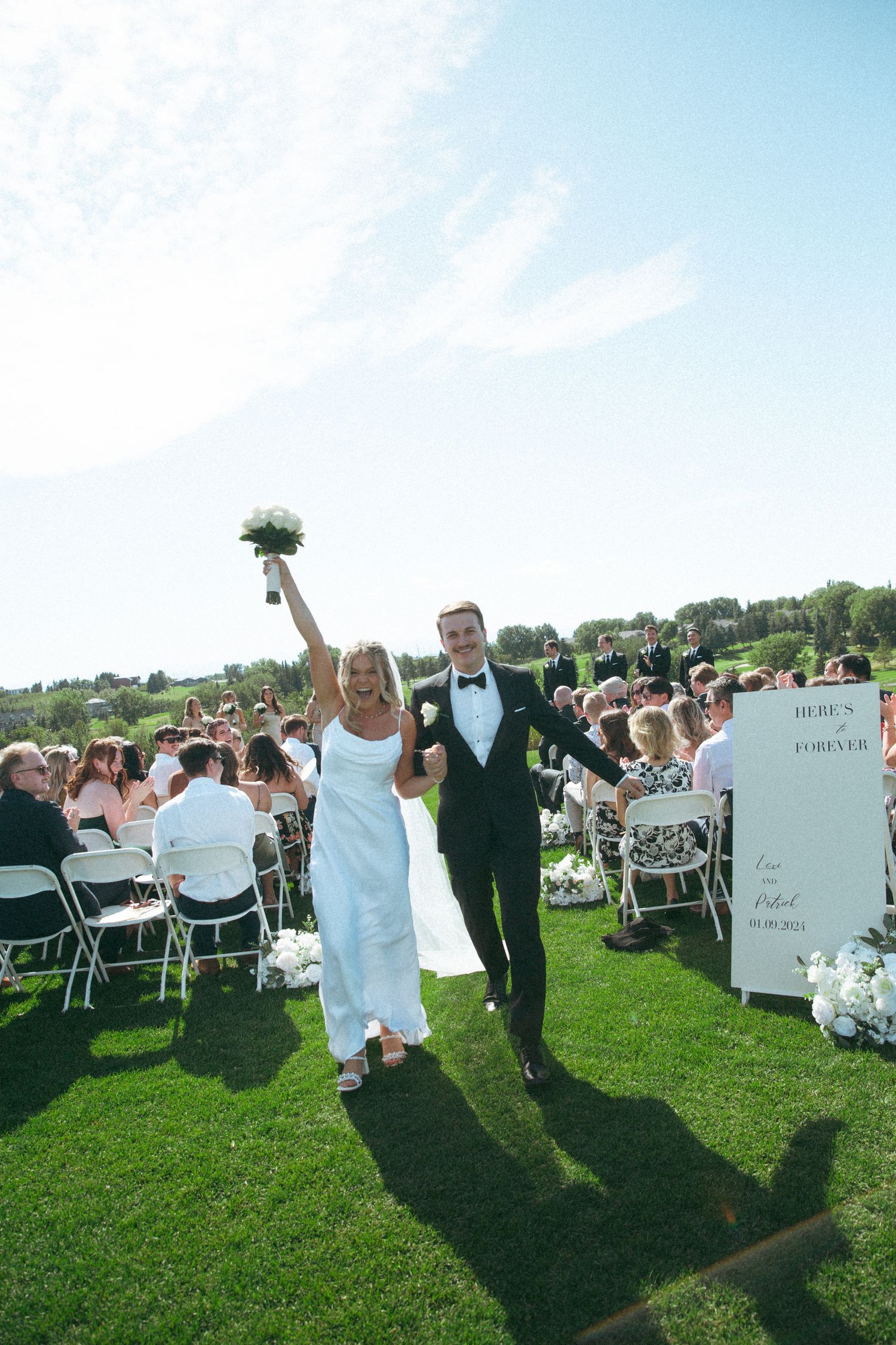 Newlyweds celebrating with raised arms while exiting outdoor wedding ceremony.