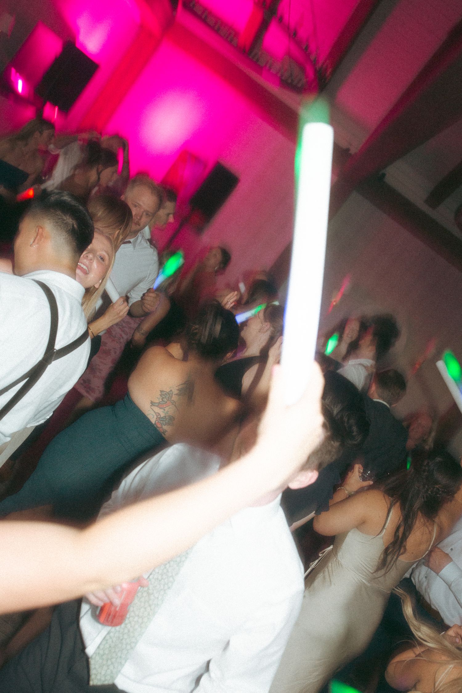 Wedding reception dance floor with pink lighting and people celebrating.