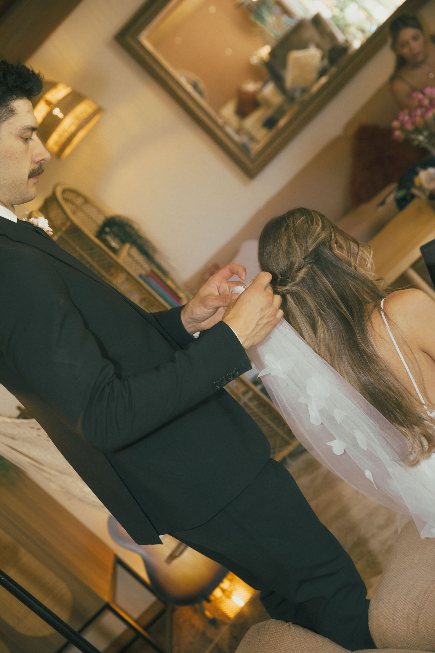Bride and groom share their first dance, with wedding veil and dark suit visible in warmly lit reception venue.