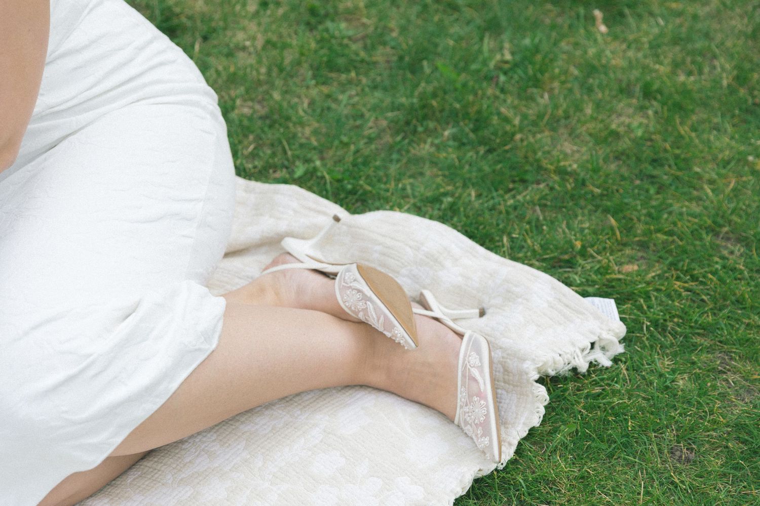 Delicate white lace fabric draped over grass in a soft, romantic outdoor setting.