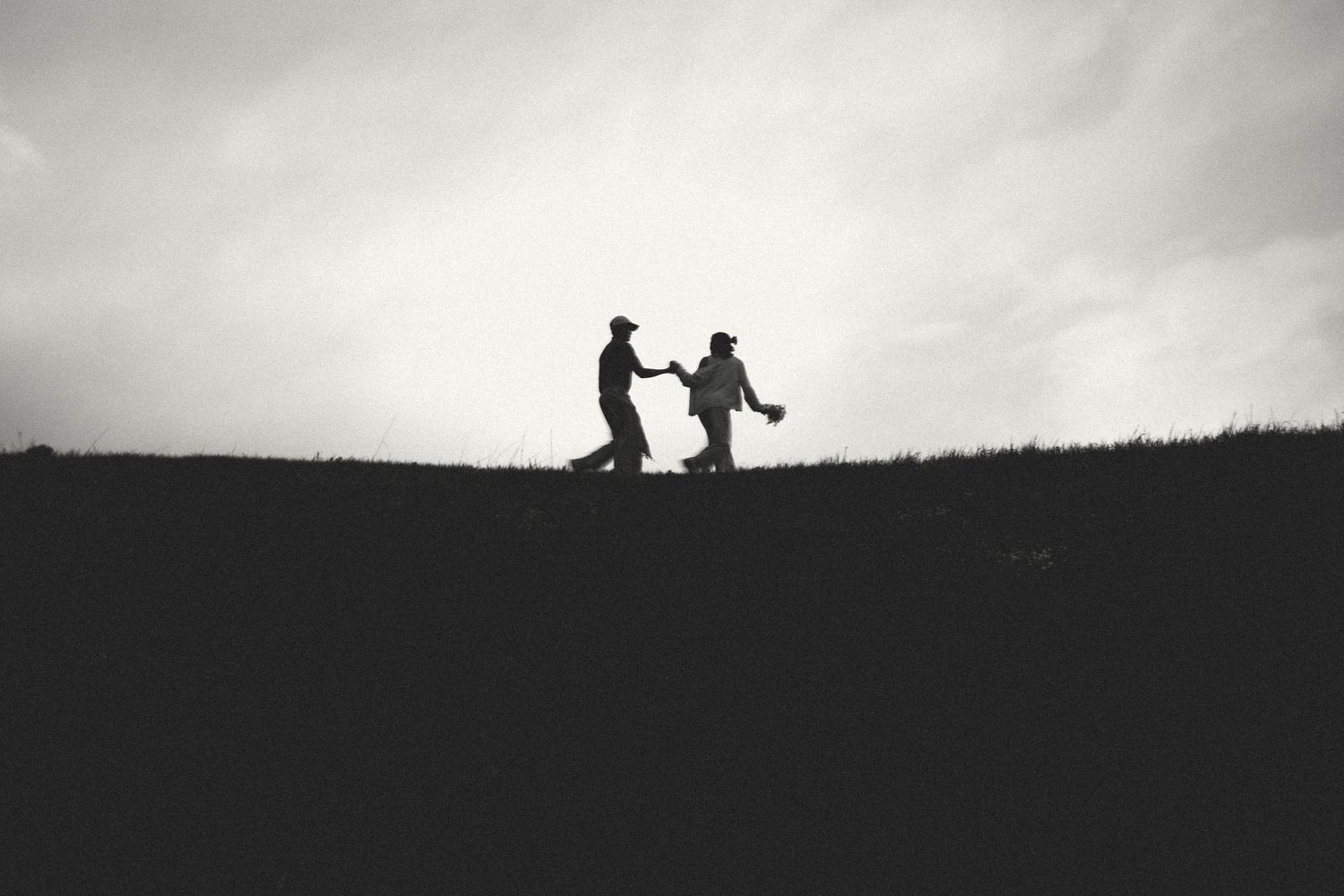 Silhouetted figures dancing together on a hilltop against an overcast sky.