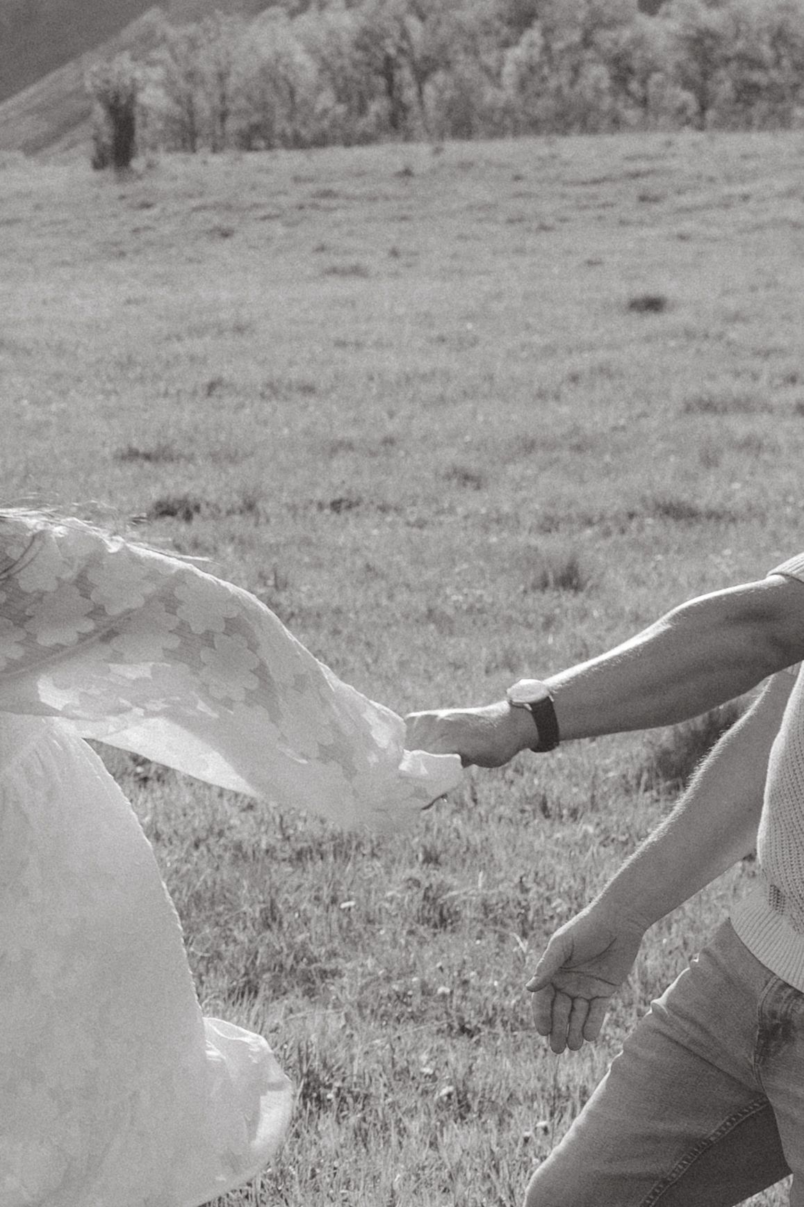 Black and white photo of two people holding hands in a grassy mountain field.