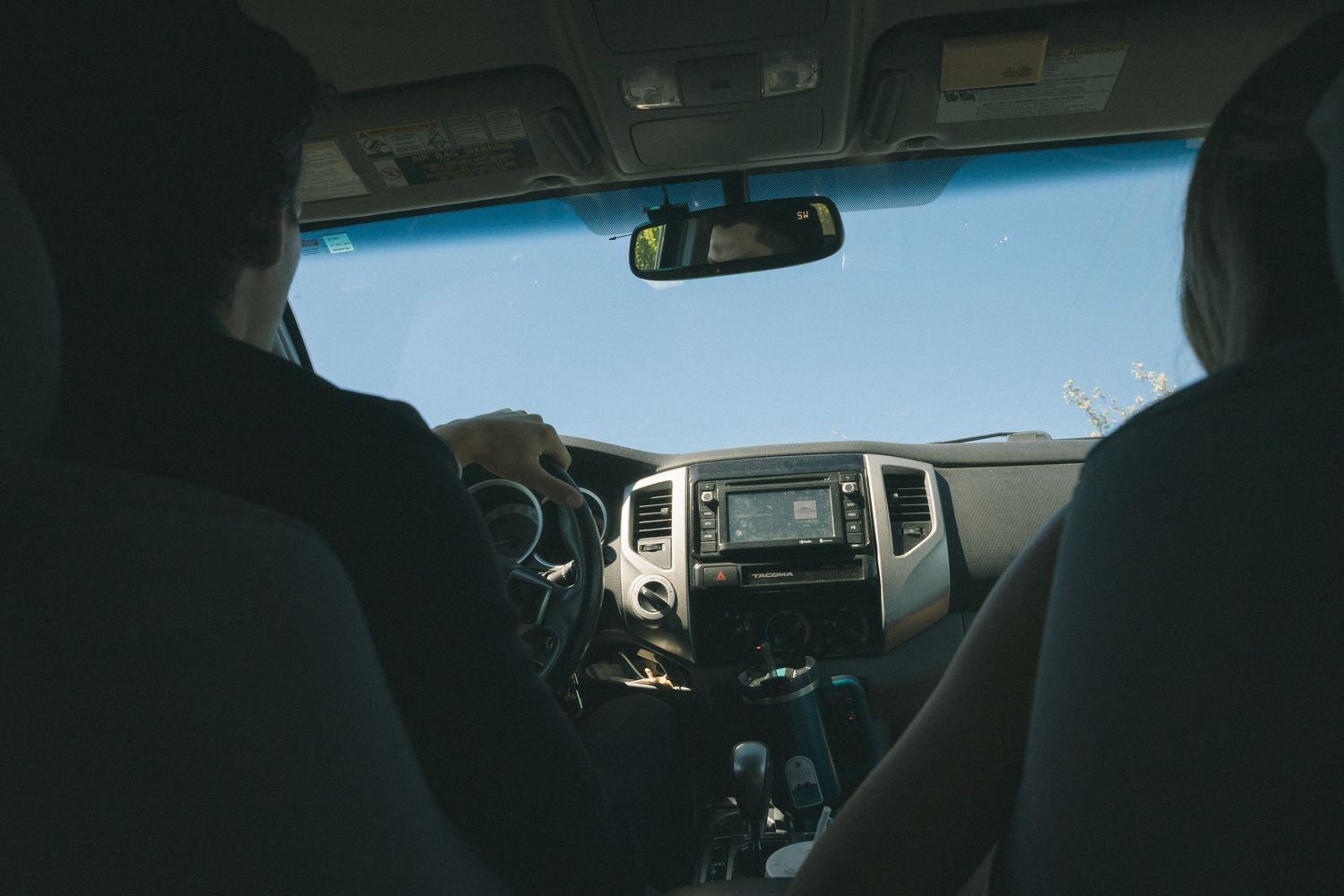 View from back seat of couple driving in SUV on sunny day.