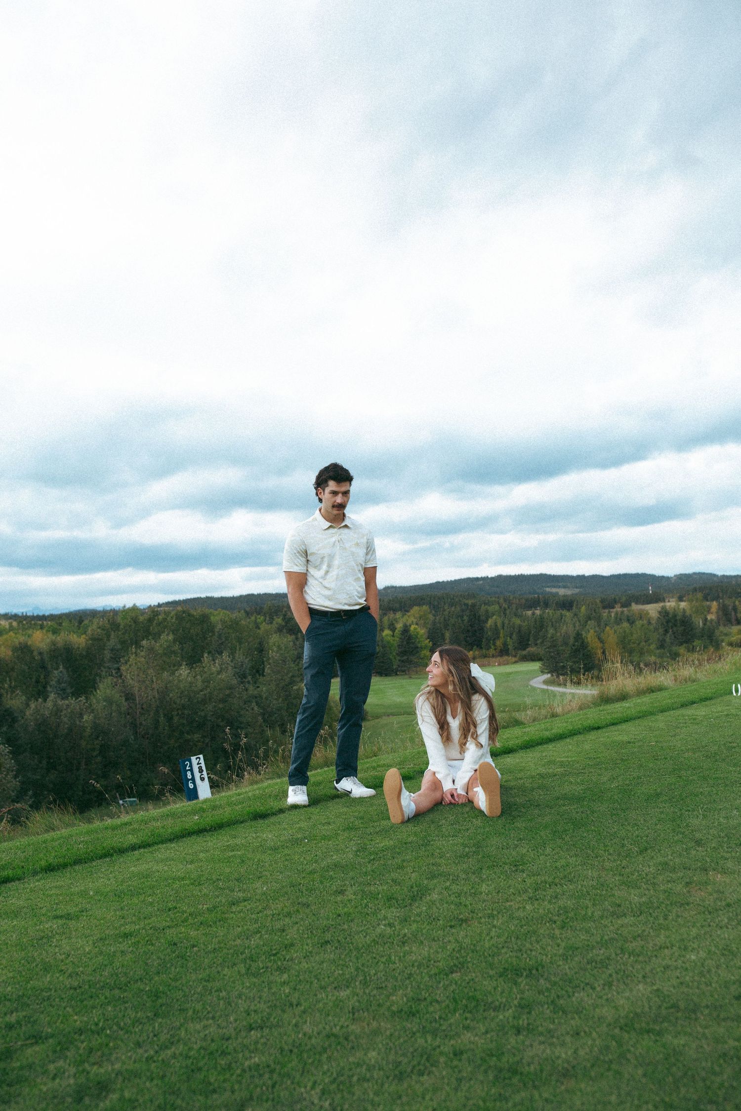 Couple enjoying a scenic view from elevated position on golf course with cloudy sky.