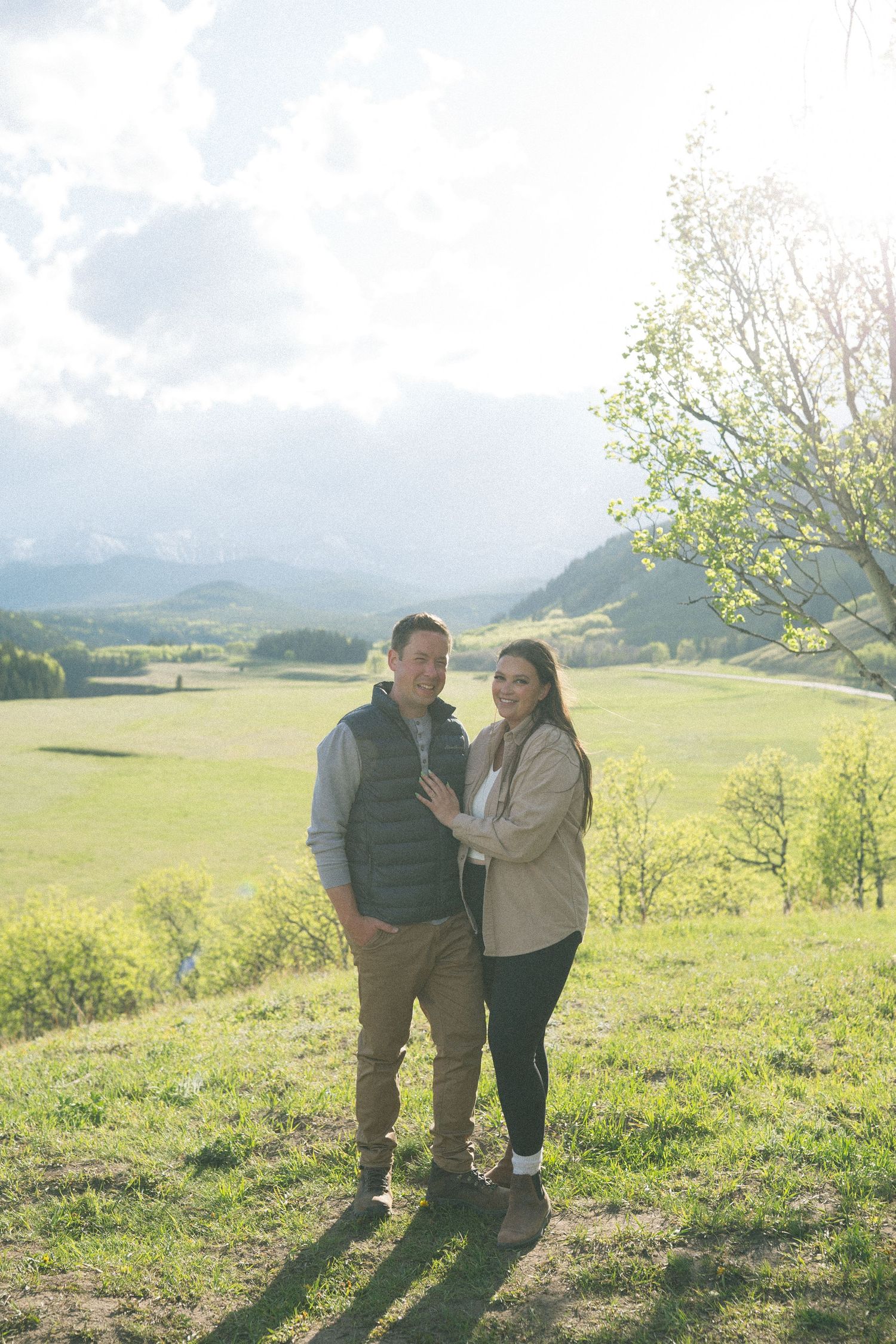 Couple standing together on hilltop overlooking scenic mountain valley on sunny day.