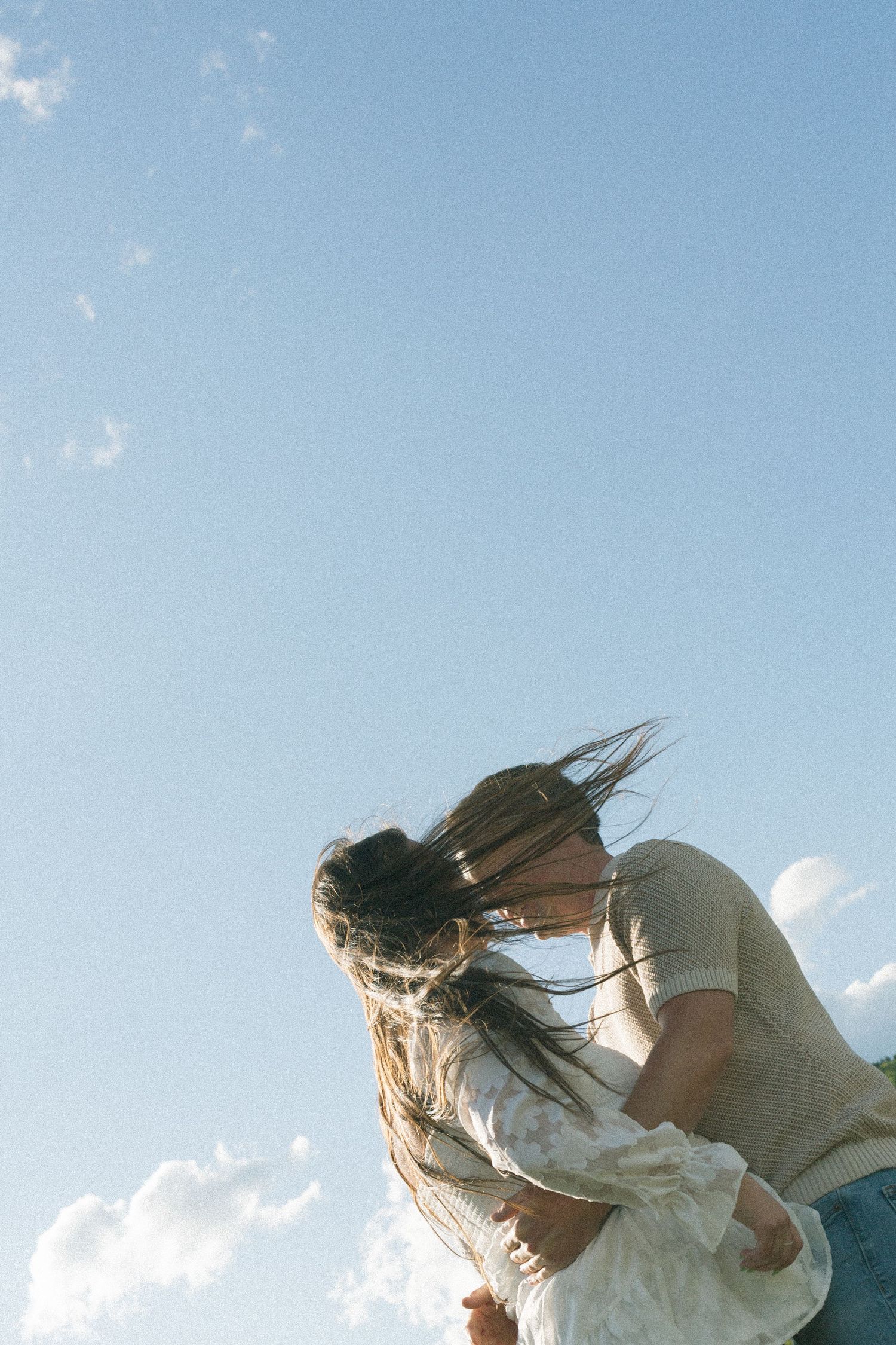 Two people sharing an intimate moment against a bright blue sky with wispy clouds.