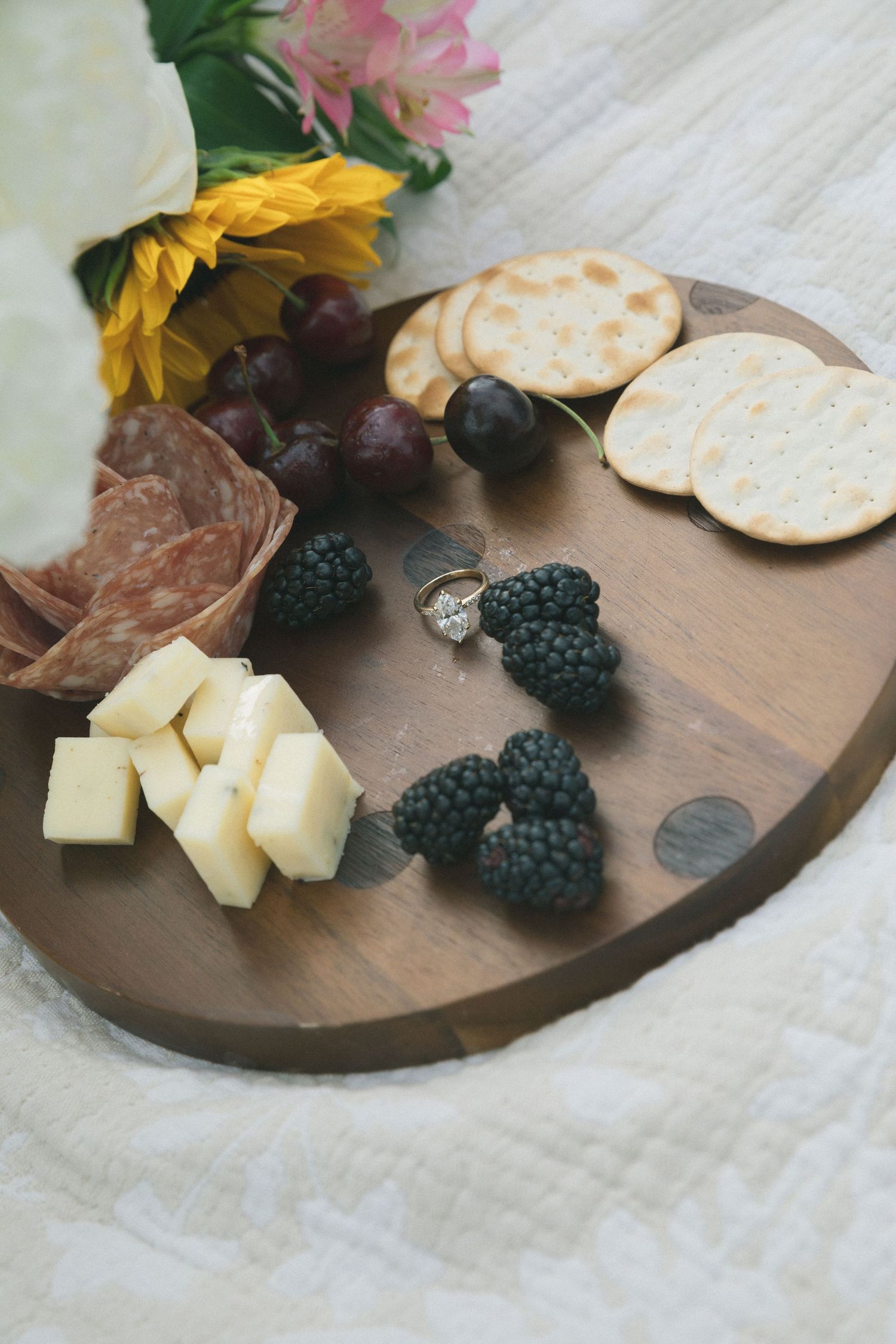 A wooden charcuterie board with cheese, blackberries, and flowers arranged artfully.