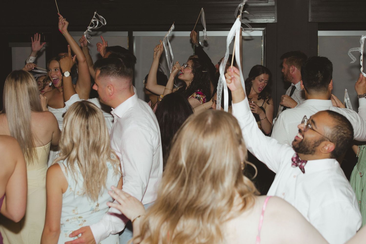 Guests dancing and celebrating at a lively wedding reception, waving ribbons in the air.