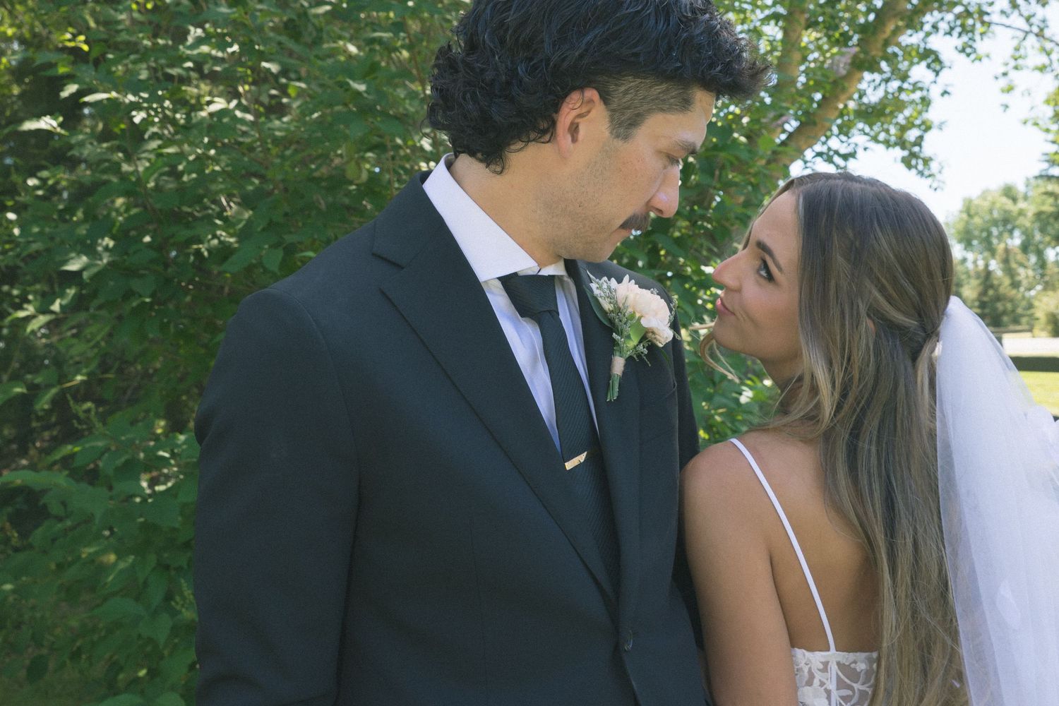 Bride and groom share an intimate moment outdoors, with the groom in a black suit and bride in a white veil.