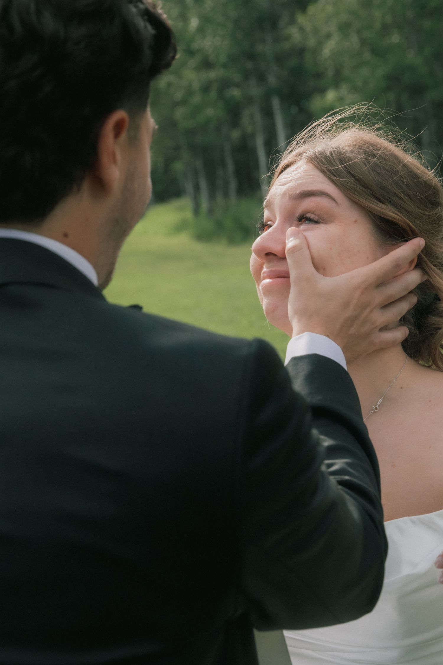 Emotional wedding moment as a groom gently wipes tears from his smiling bride's face outdoors.
