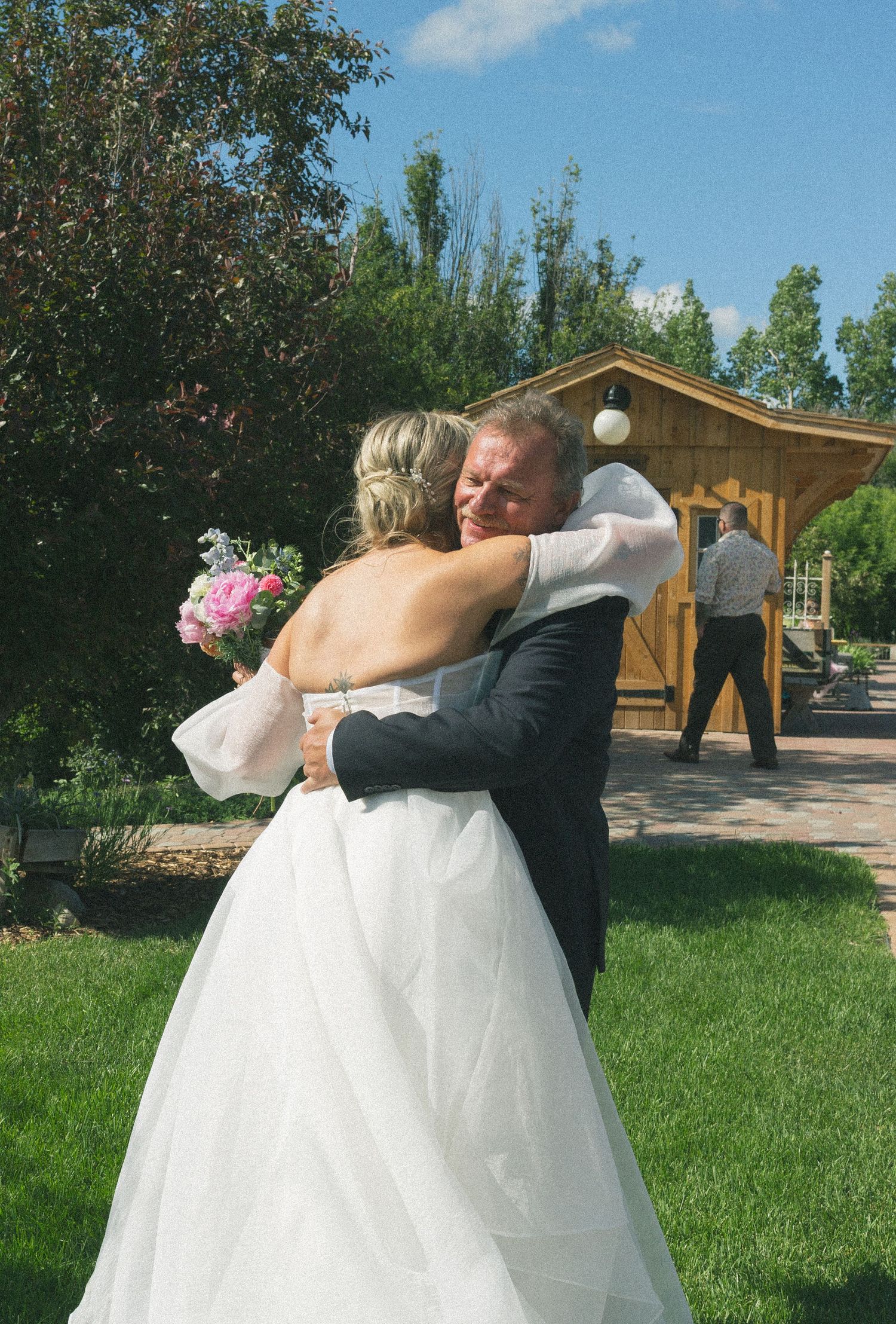 Couple shares an intimate moment on manicured lawn with wooden building in background.