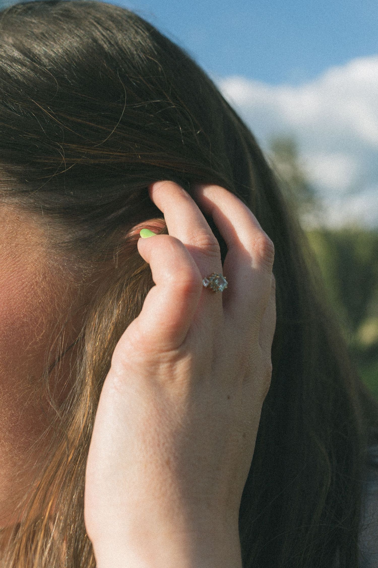 Close-up of a sparkling engagement ring on hand with blue sky and clouds in background.
