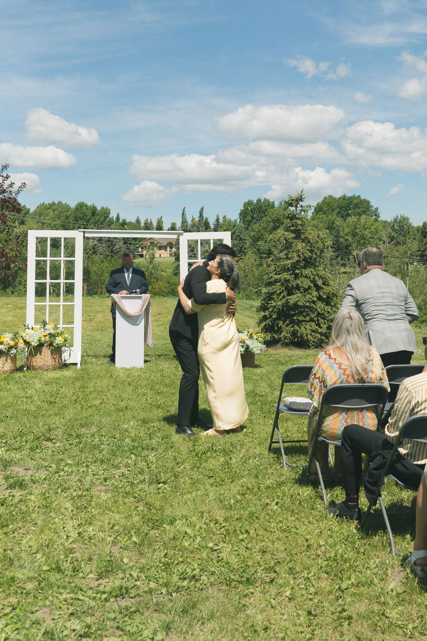 Couple sharing a first kiss at an outdoor wedding ceremony with white door arch and seated guests.