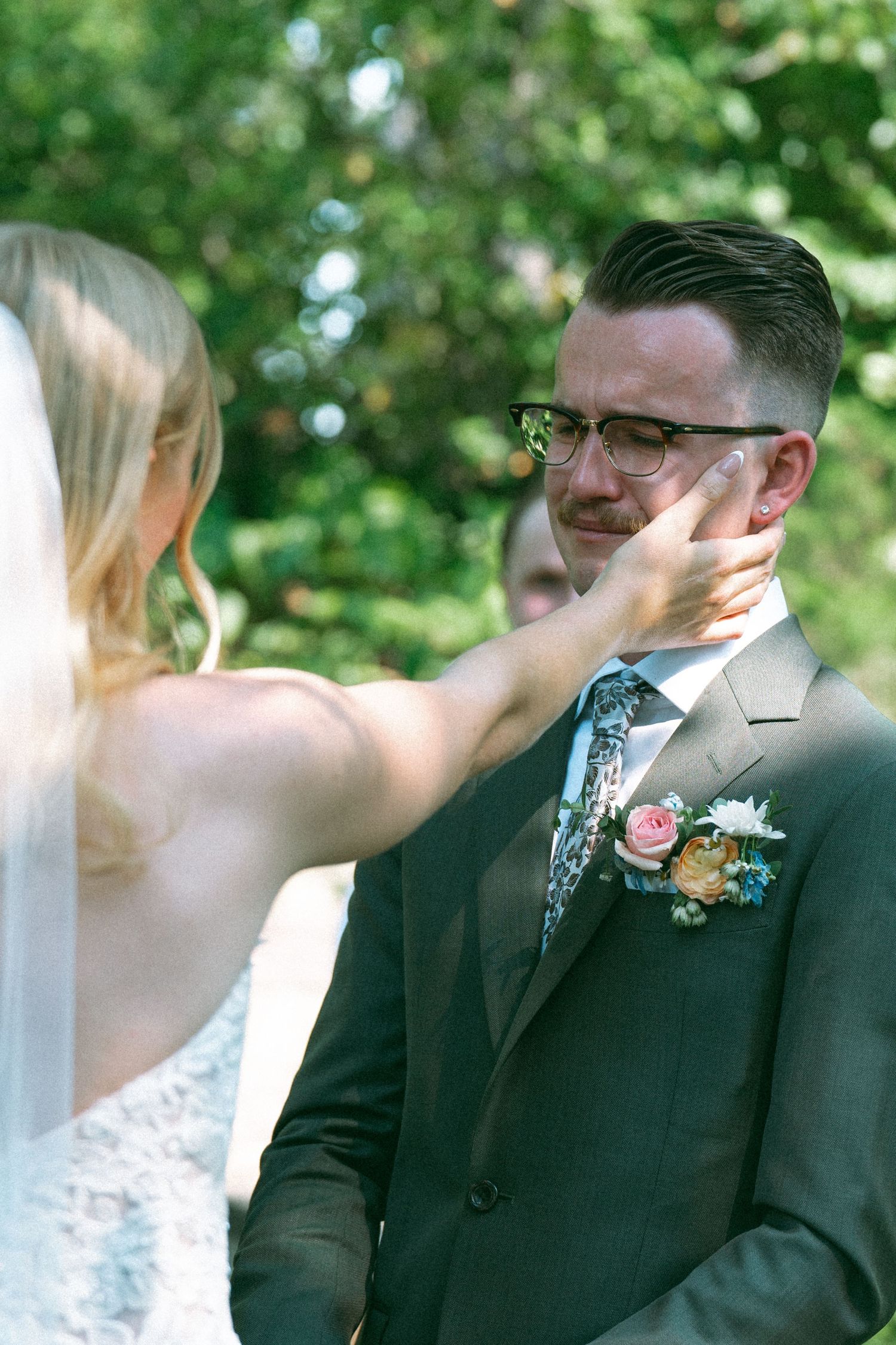 A tender moment at an outdoor wedding ceremony with a floral boutonniere and elegant attire.