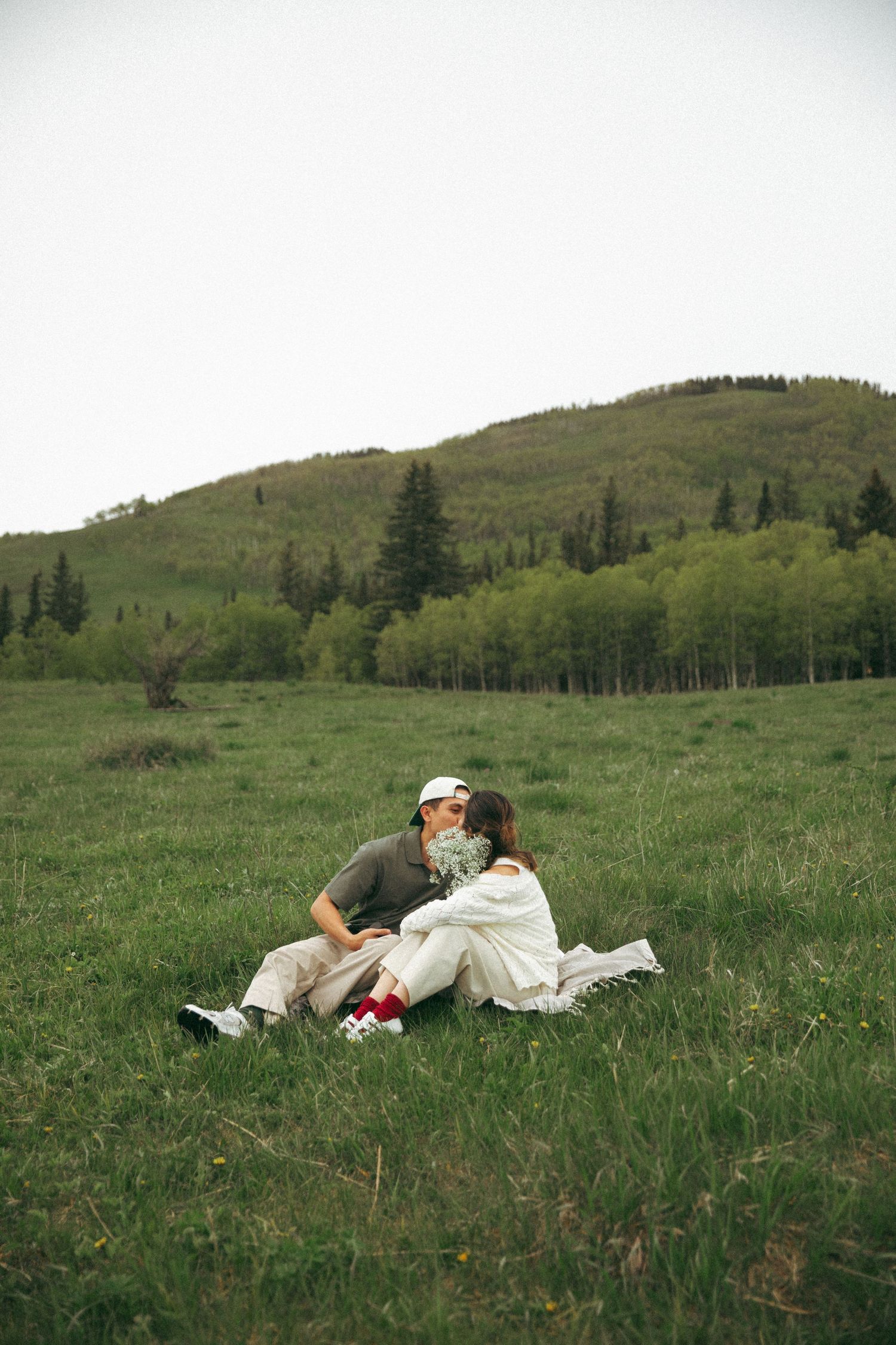 Couple having romantic picnic on grassy hillside overlooking mountain landscape.