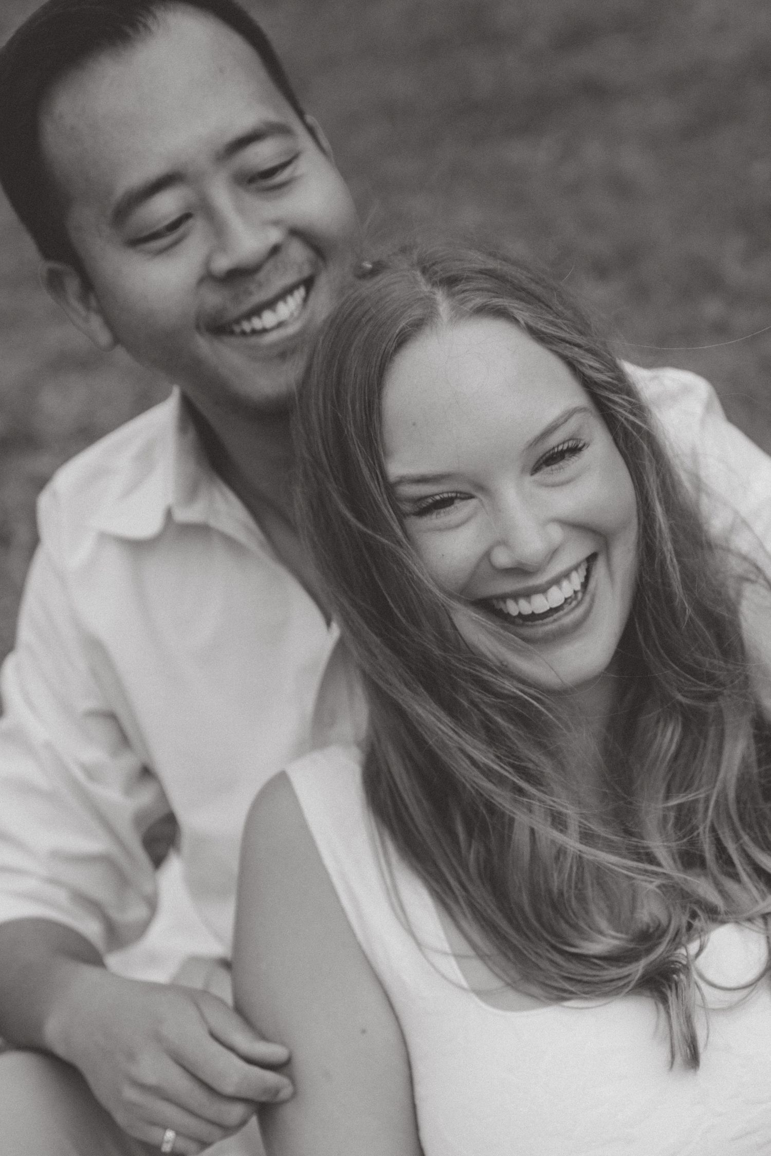 A joyful couple sharing a candid black and white laughing moment together outdoors.