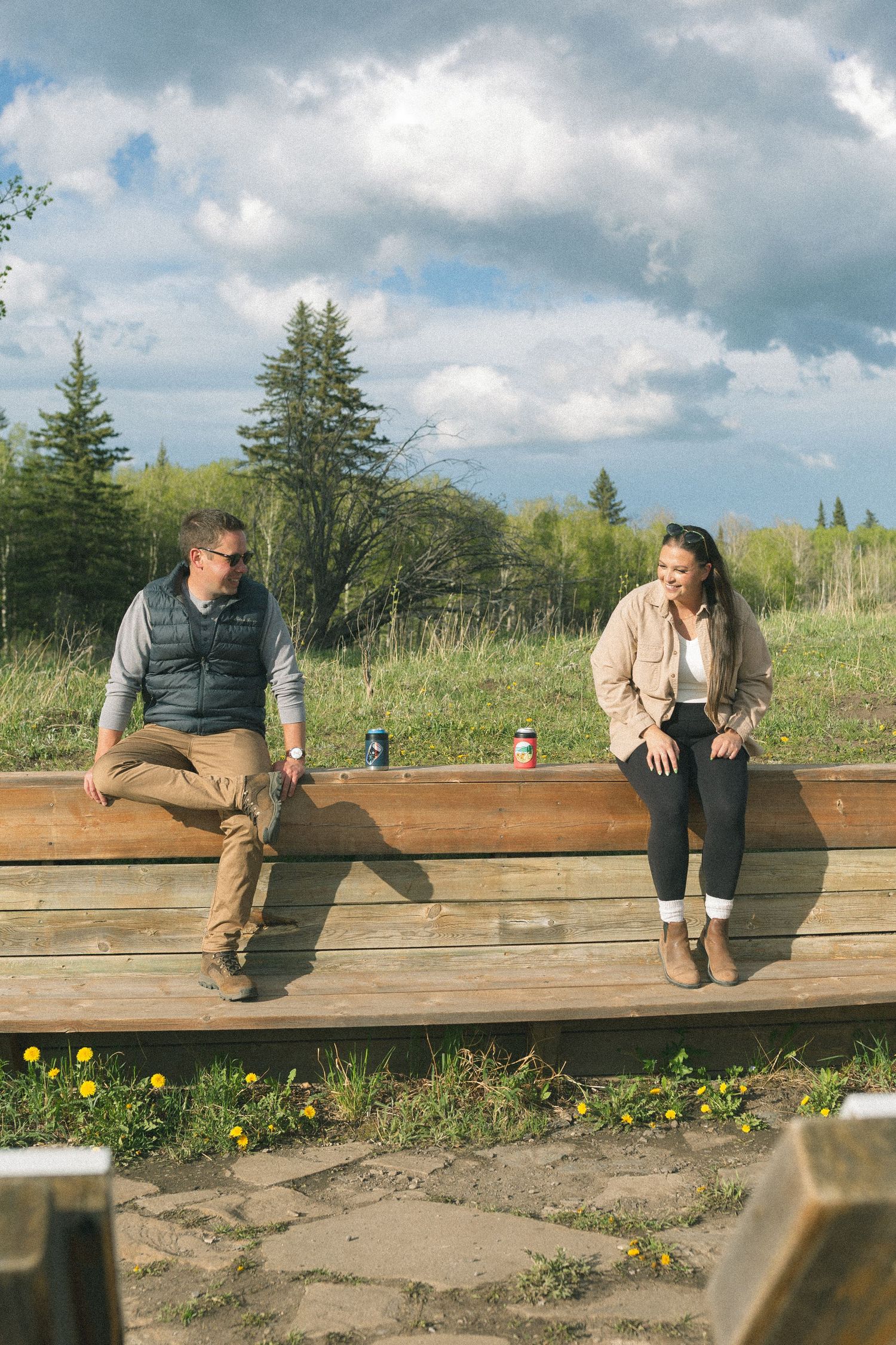 Two people sitting on wooden bench enjoying mountain views under cloudy skies.