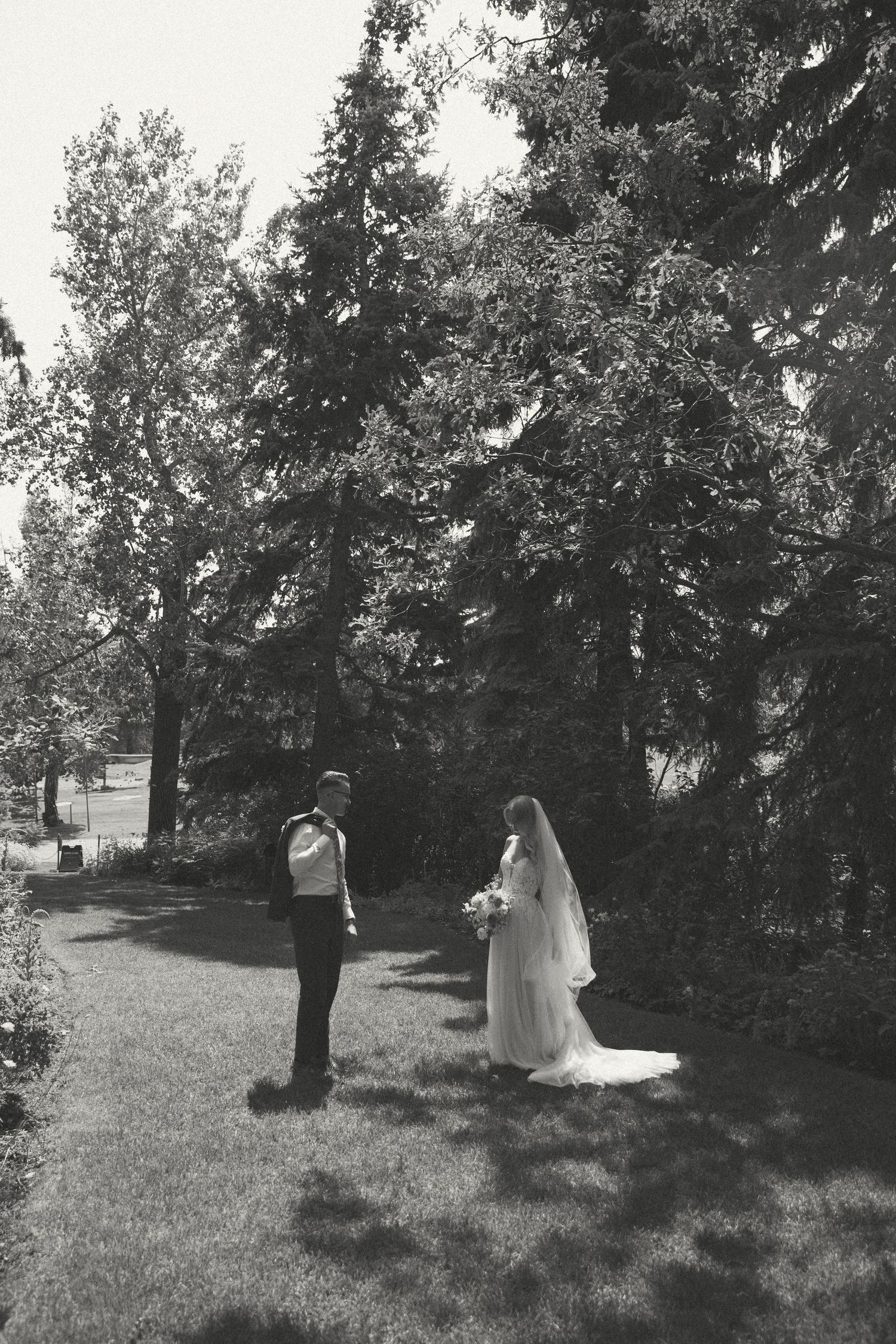 Black and white wedding photo of couple standing in a serene garden path.