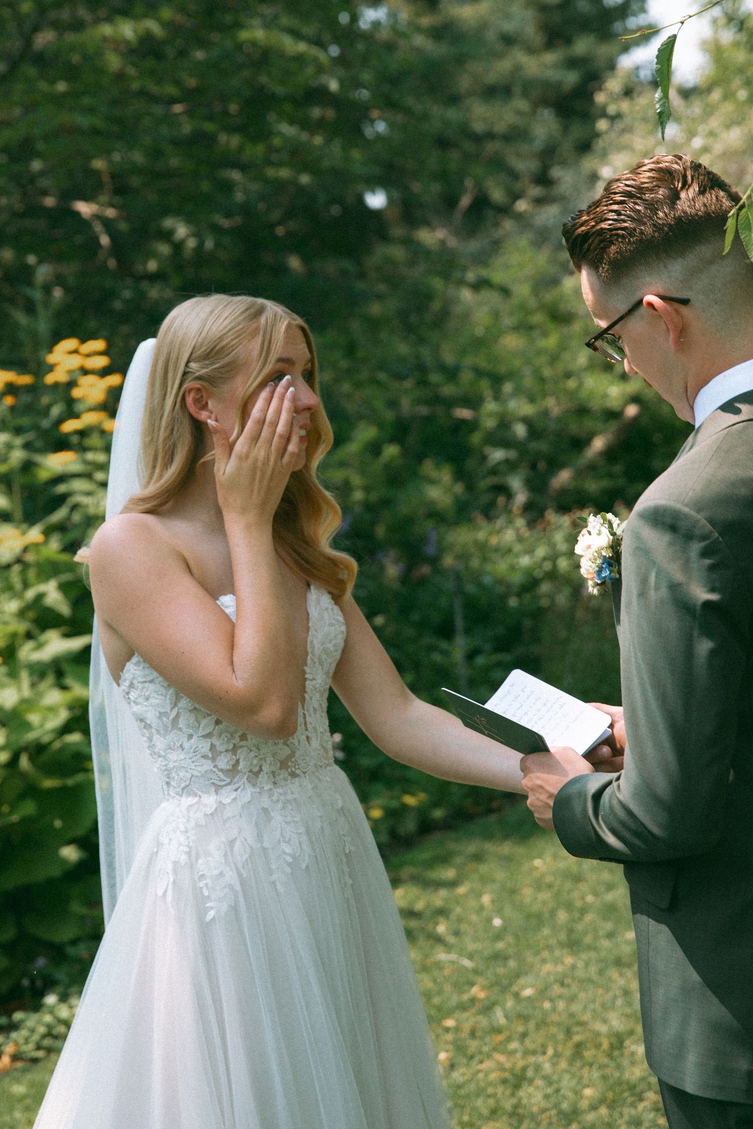 An emotional moment during wedding vows in a garden setting with yellow flowers.