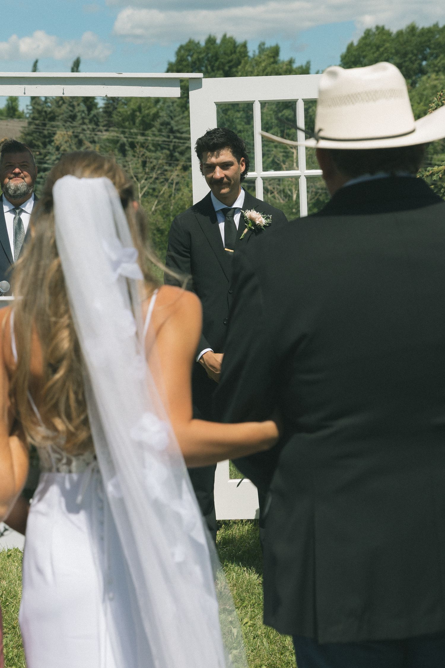 Groom smiling at bride walking down the aisle at outdoor wedding ceremony.