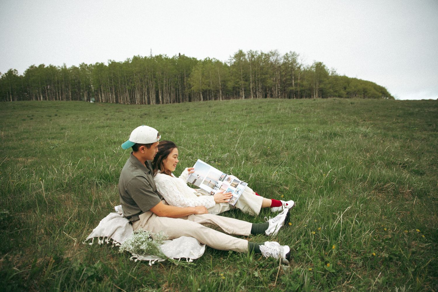 Two people relaxing together on a green hillside on a cloudy day.
