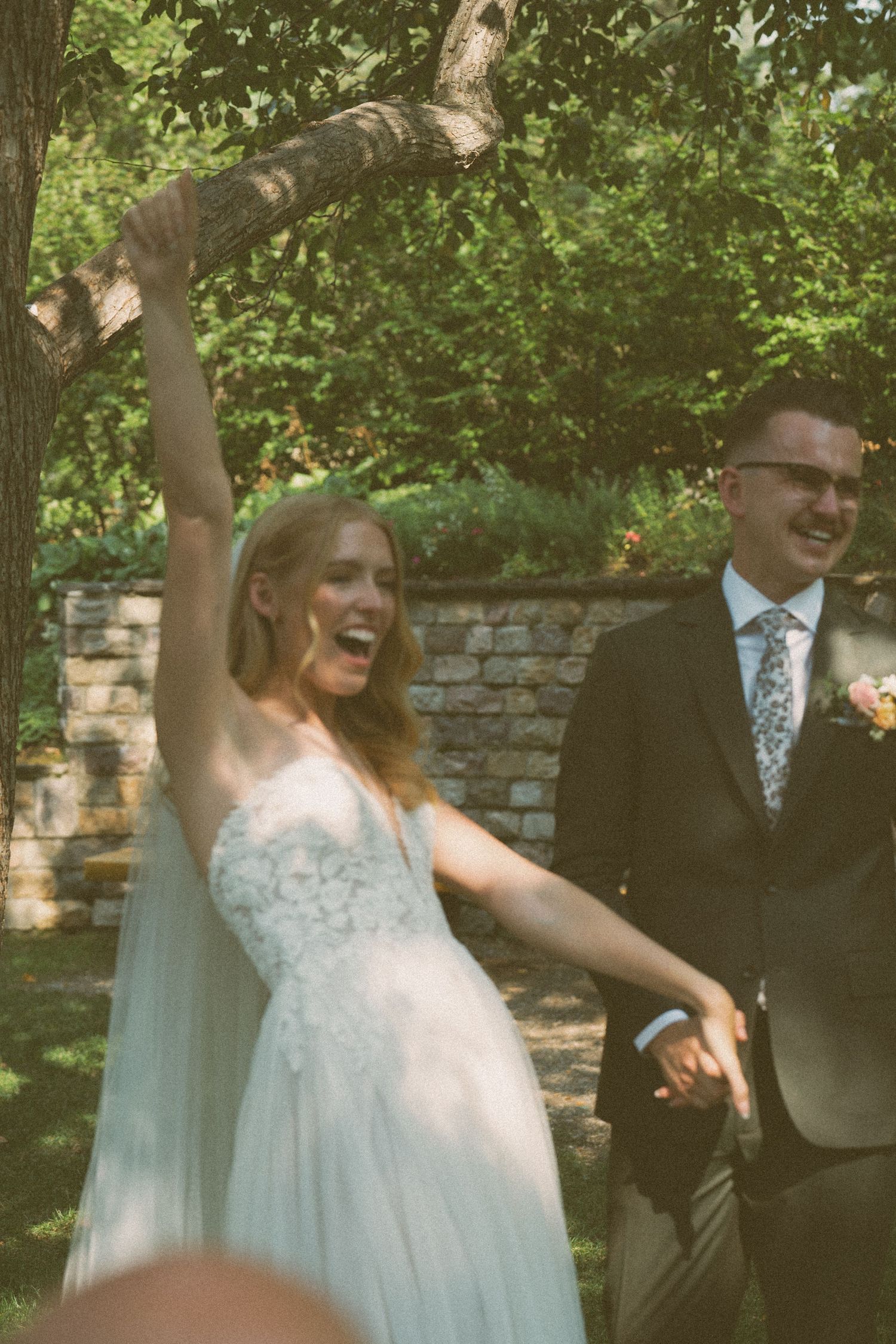 A joyful outdoor wedding celebration in a garden setting with greenery and a brick wall backdrop.
