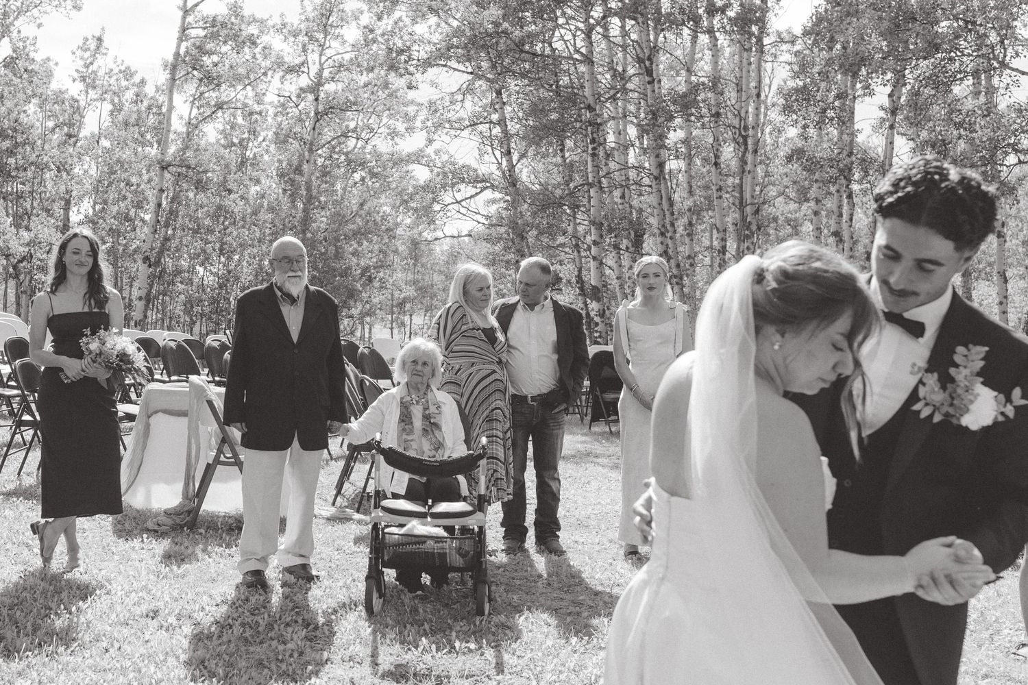 Black and white wedding photo of bride and groom dancing while guests watch outdoors.