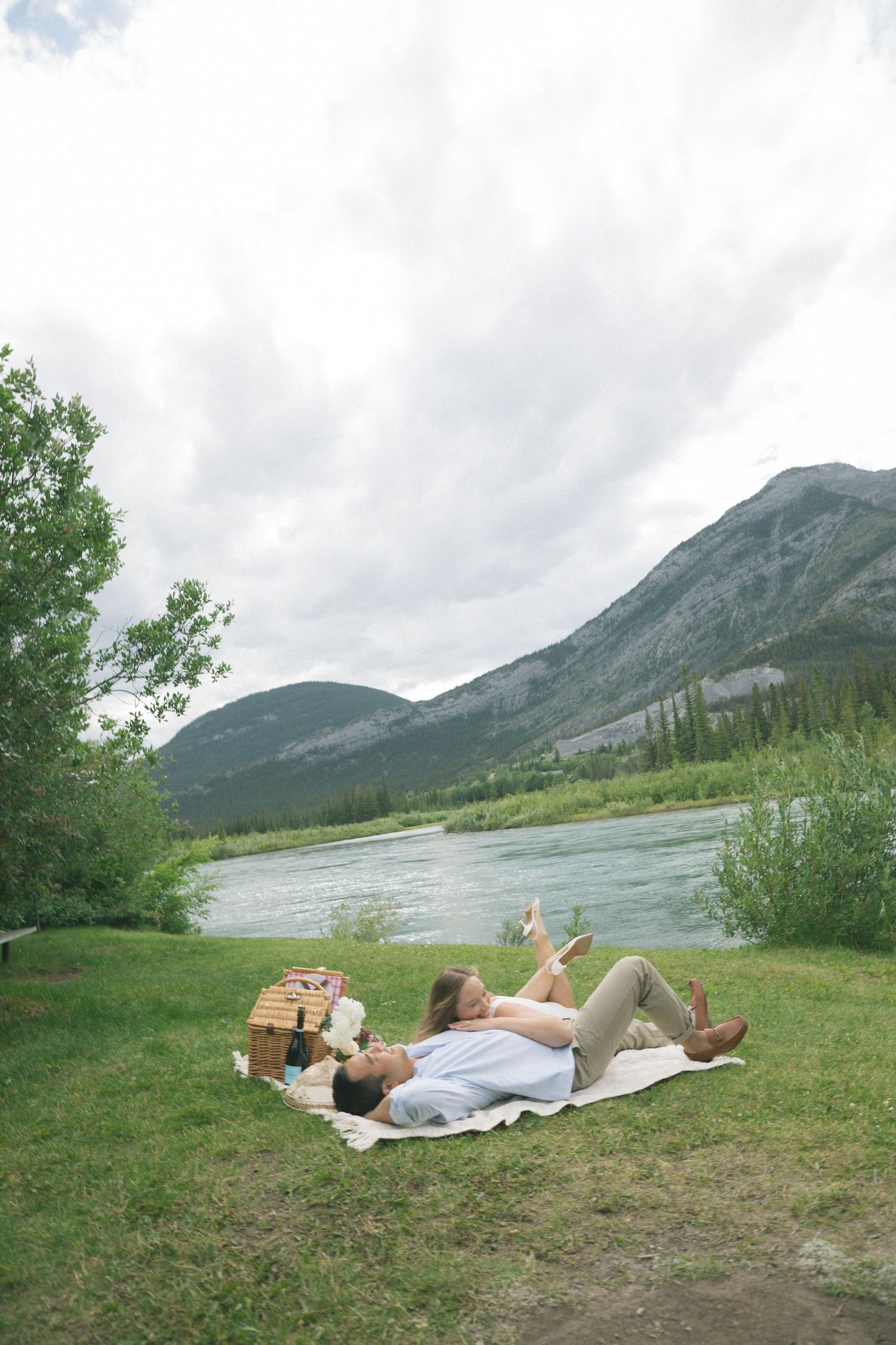 Scenic picnic setting by a mountain lake with couples relaxing on blankets against dramatic landscape views.