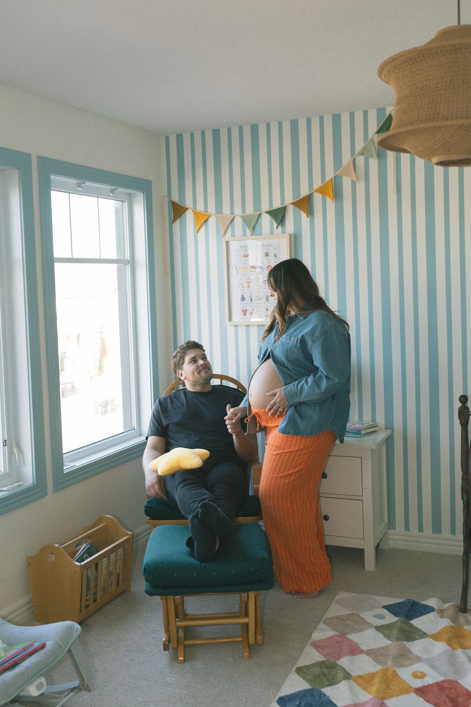 People sitting in a room with blue and white striped wallpaper, featuring chairs and a decorative quilt pattern.