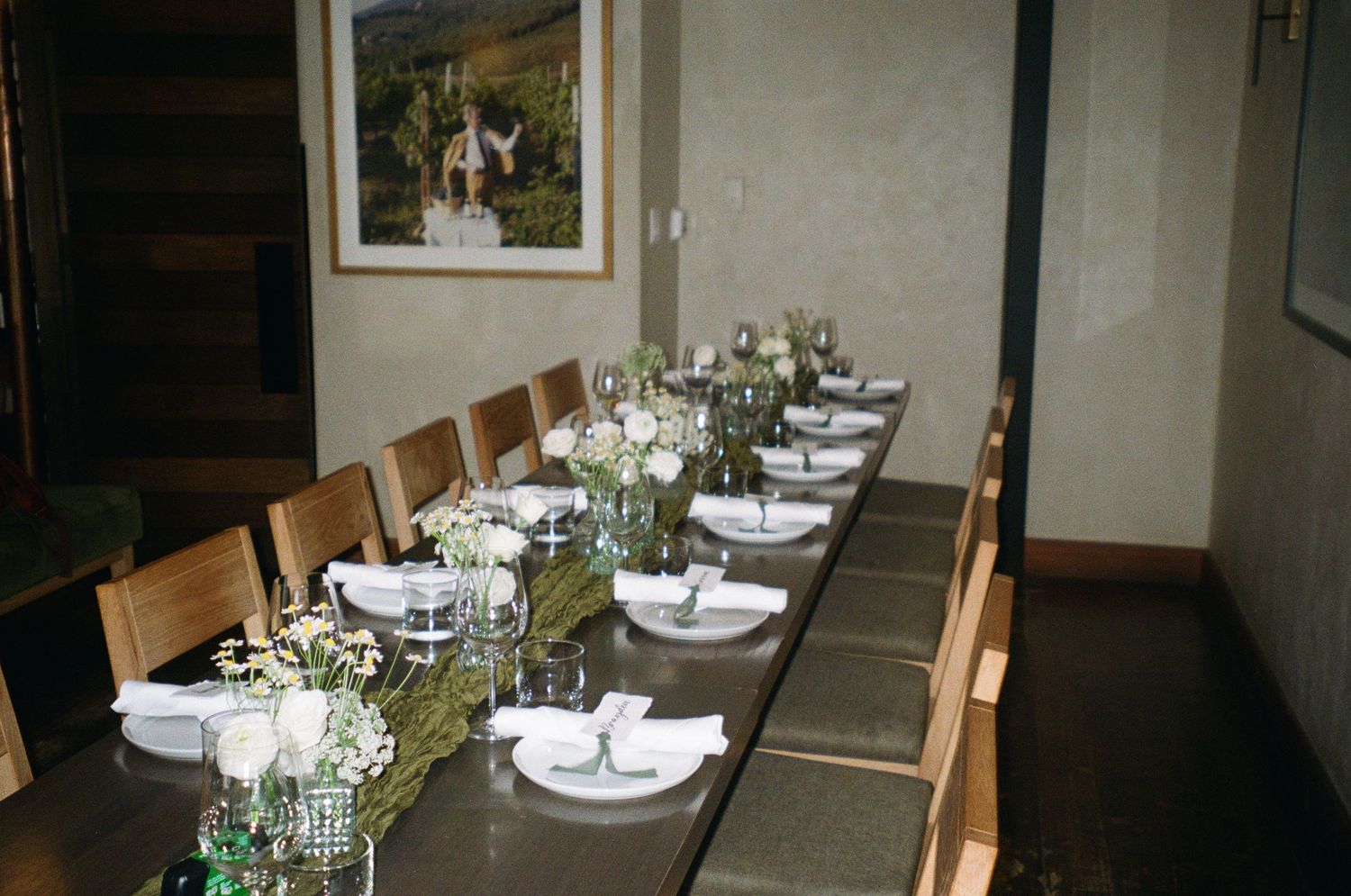 A long dining table set with white plates and green floral centerpieces in a modern restaurant interior.